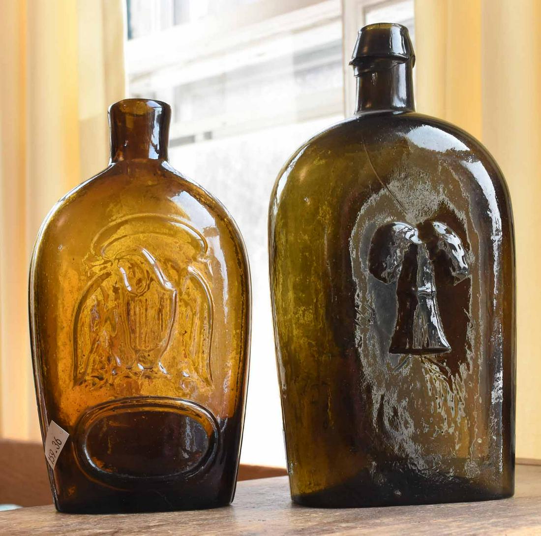 Two Early Glass Flasks: Two early glass flasks, amber double eagle, 7.5” x 4”, with olive green “Traveler’s Companion”, with sheaves of wheat on other side, 8.75”H x 4.5”W.