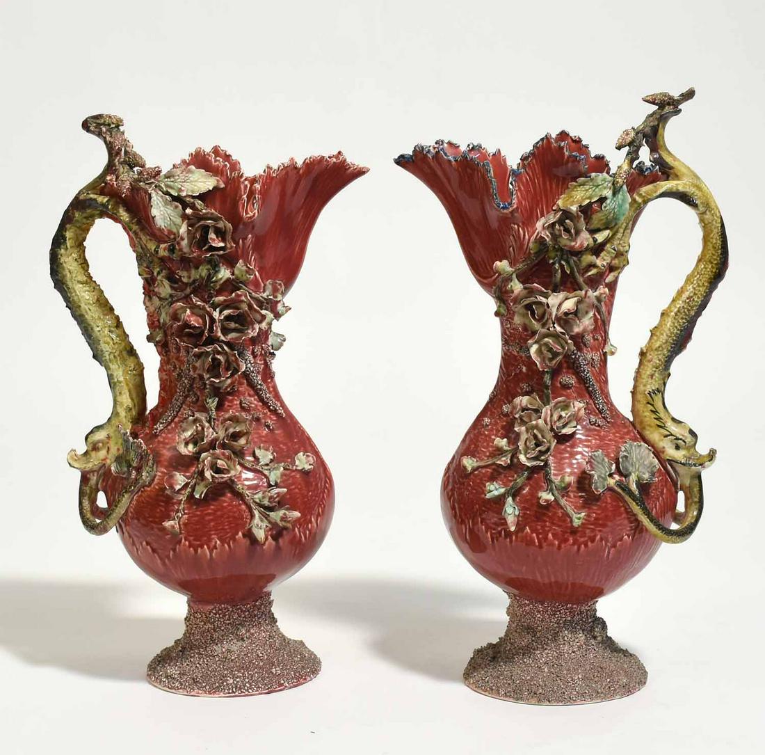 Pair of Large French Majolica Ewers: Pair of French majolica ewers with dolphin form handles and applied floral decoration, 18”H x 8”W.