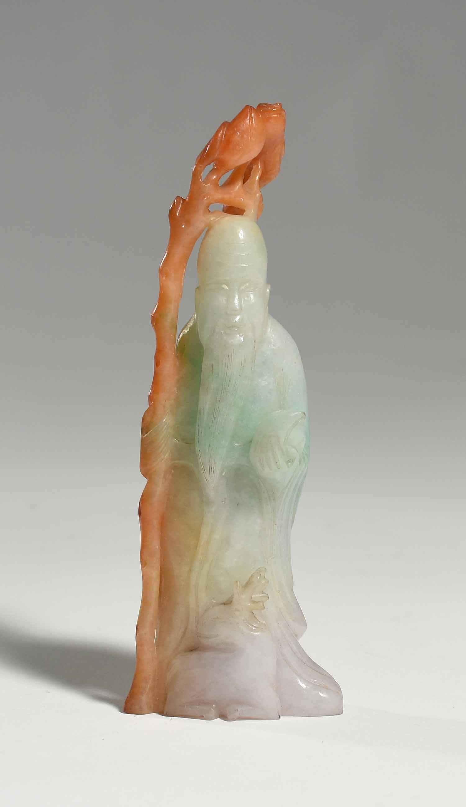 Jade Carving of Elder Figure: Multi-colored jade carving of elder figure holding staff and fruit, with deer at feet. Staff in russet color. 5.25”H x 1.75”W. 