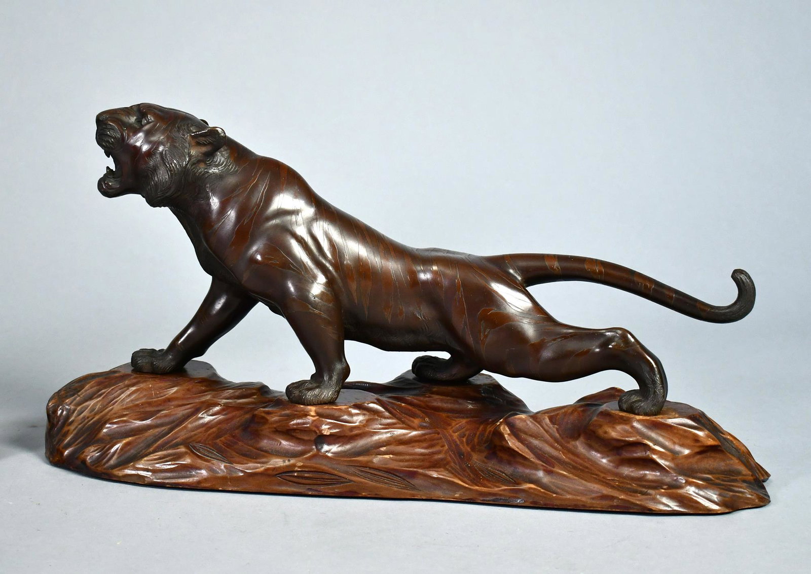 JAPANESE MEIJI BRONZE TIGER.: A Japanese Meiji stalking bronze tiger with glass eyes, an open mouth and a curled tail, signed on underside of stomach in Japanese characters, sitting on a period wood base. Tiger 19”L x 11R