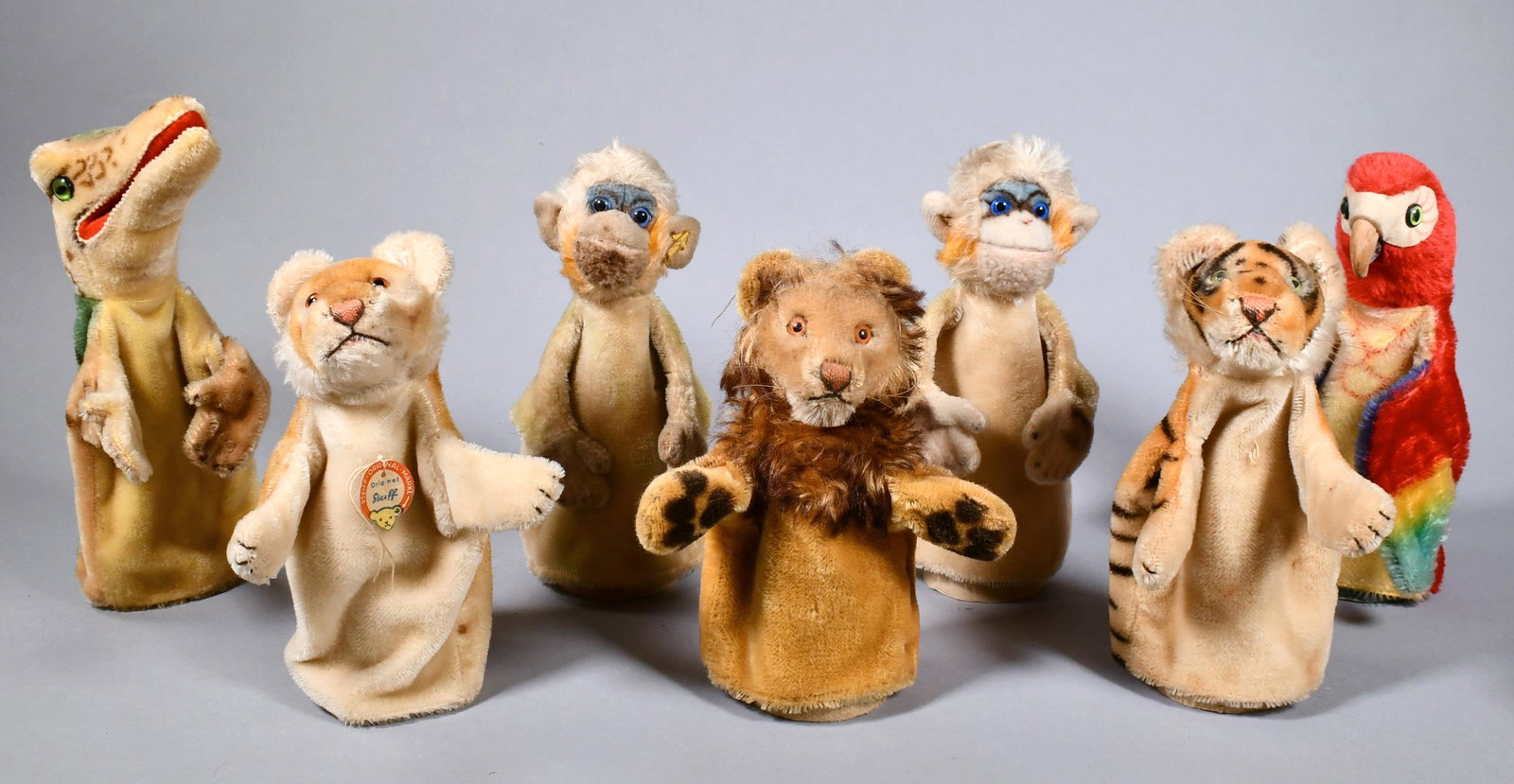 SEVEN STEIFF JUNGLE ANIMAL HAND PUPPETS.: Including a parrot, crocodile, two monkeys, a tiger, a lion, and a lioness. Puppets retain either button-in-ear, name tag collar, or evidence of either. All puppets approximately 10”H.