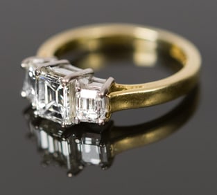 18K GOLD 3-STONE EMERALD CUT DIAMOND RING.