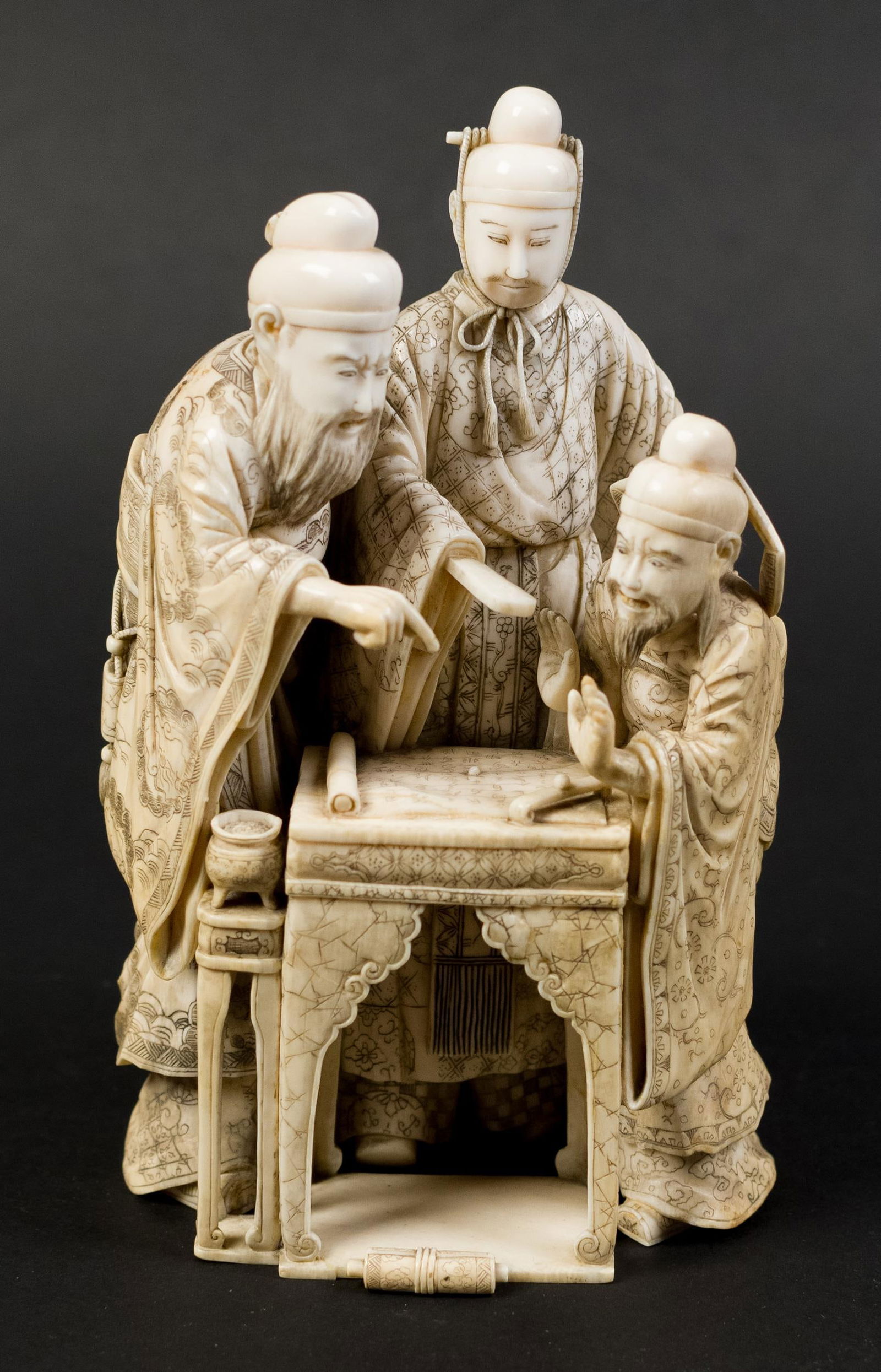 JAPANESE BONE CARVING, DIGNITARIES.: A Japanese bone carving of three dignitaries discussing a scroll laid out on a table. Signed on bottom, 7”H.
