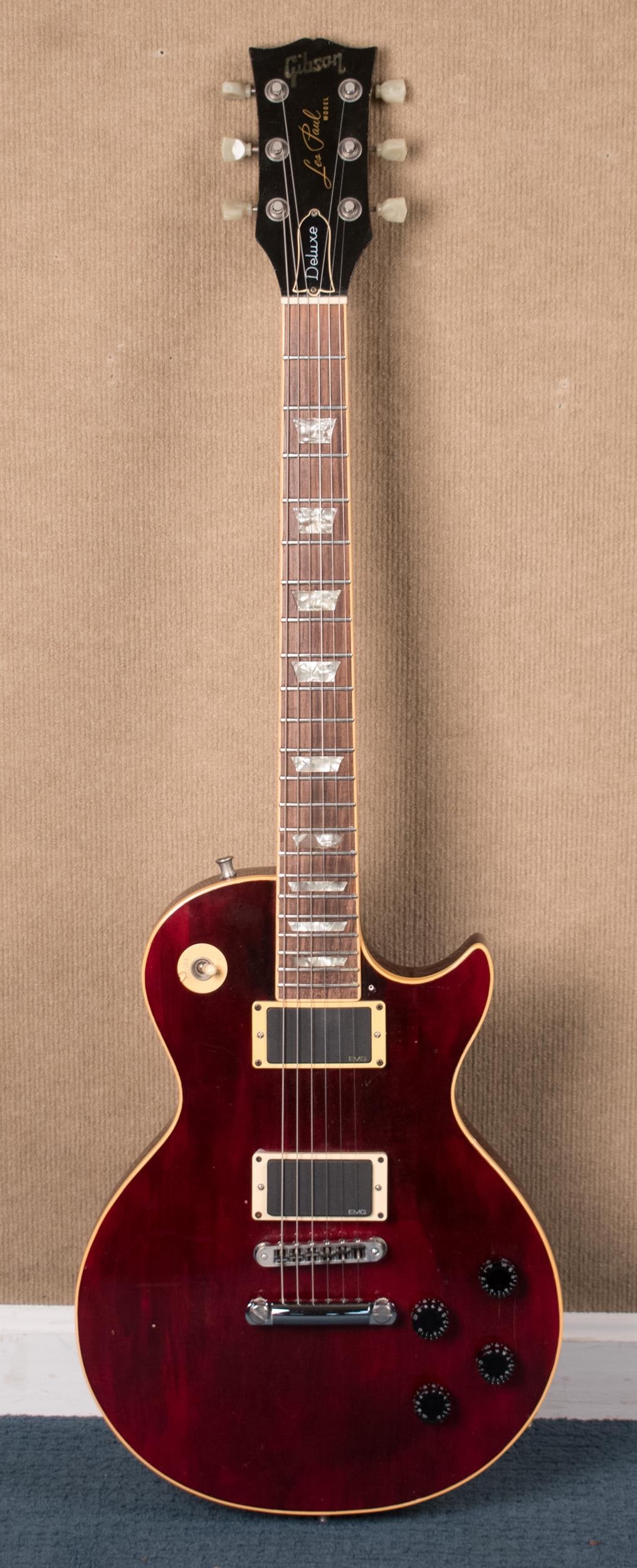 1975 GIBSON LES PAUL DELUXE GUITAR IN WINE RED.: A 1975 Gibson Les Paul Deluxe guitar in wine red with a chainsaw case. Scale length 24.75”L, Overall 39”L, Case 43”L.
