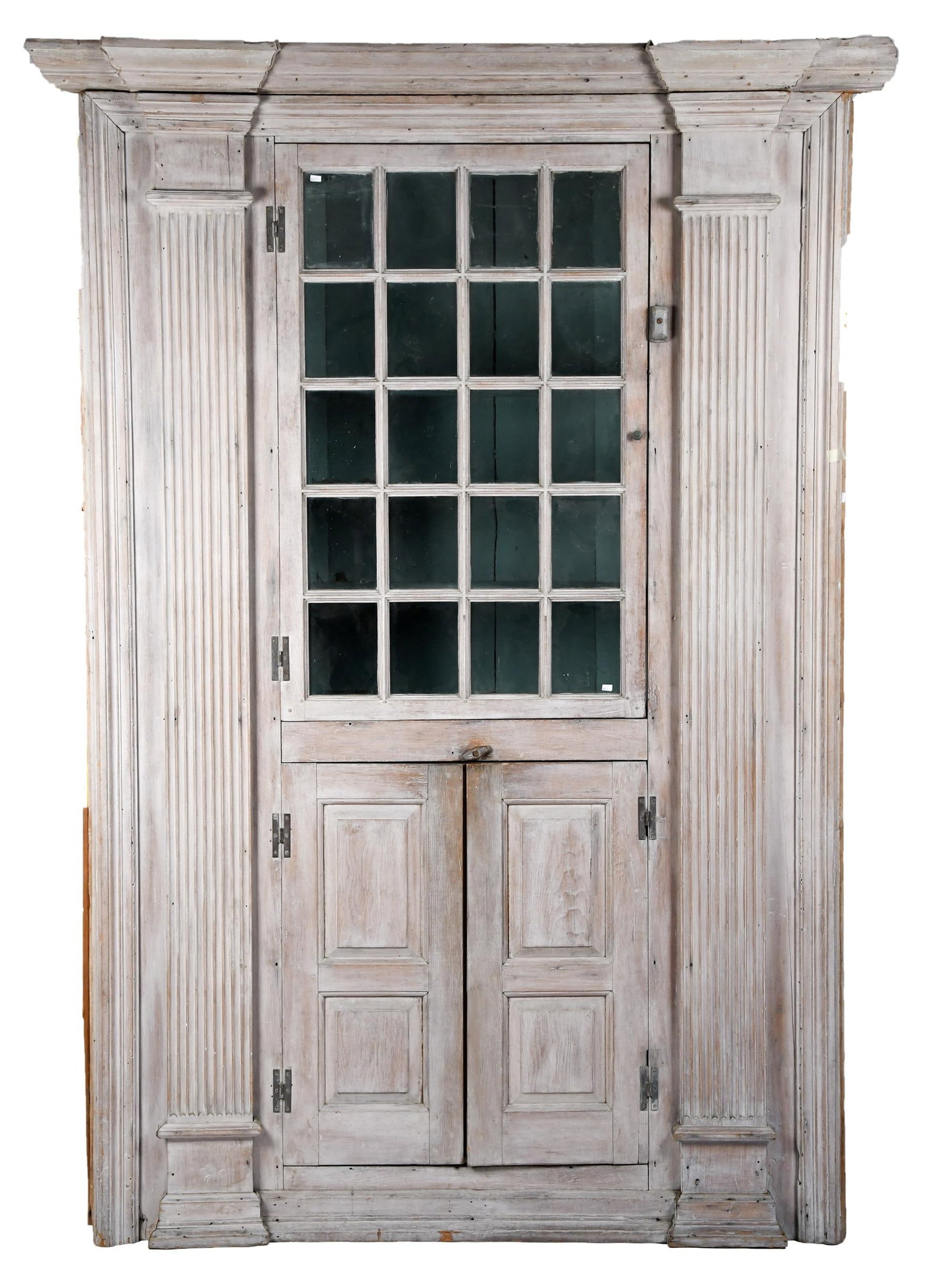 RARE MID 18TH C. ARCHITECTURAL PINE CORNER CUPBOARD.: A mid 18th C. New England architectural pine corner cupboard with unusual desk interior, having a boldly stepped cornice molding above a twenty-light single door, above two raised panel doors, flanked