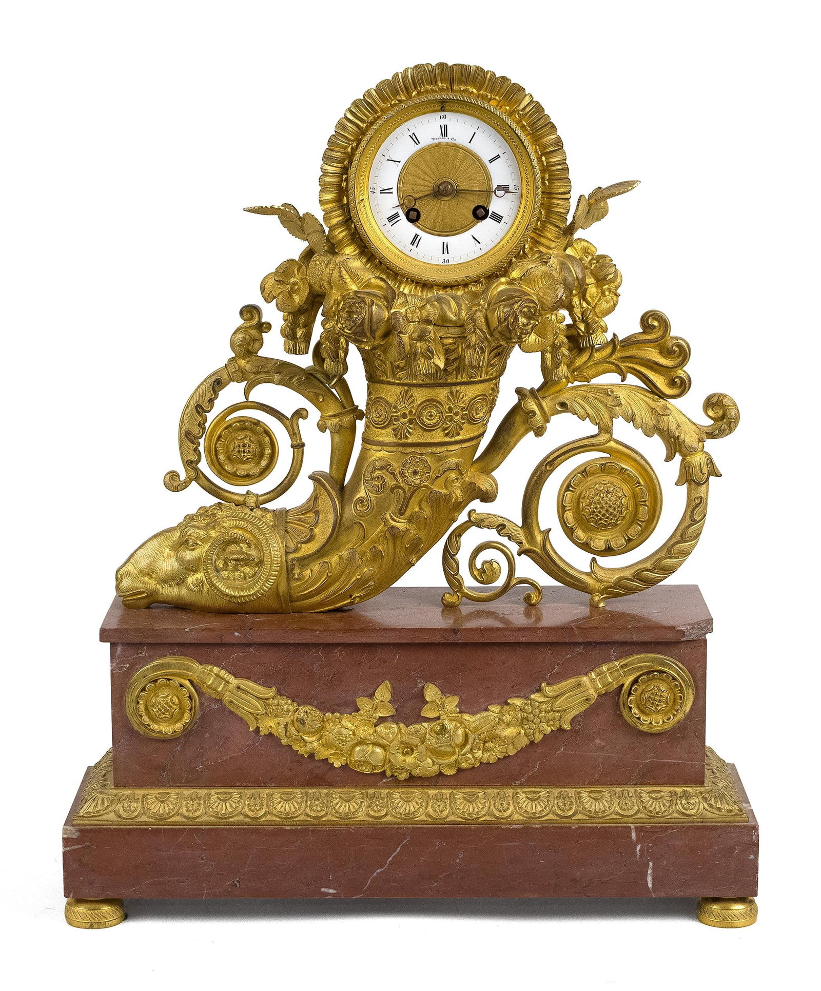 FRENCH EMPIRE BRONZE AND MARBLE CLOCK, TIFFANY & CO.: A 19th C. Tiffany & Co. French Empire style gilt bronze mantle clock, rams head cornucopia design, with a painted porcelain dial signed Tiffany & Co., and base in red marble with gilt bronze decoratio