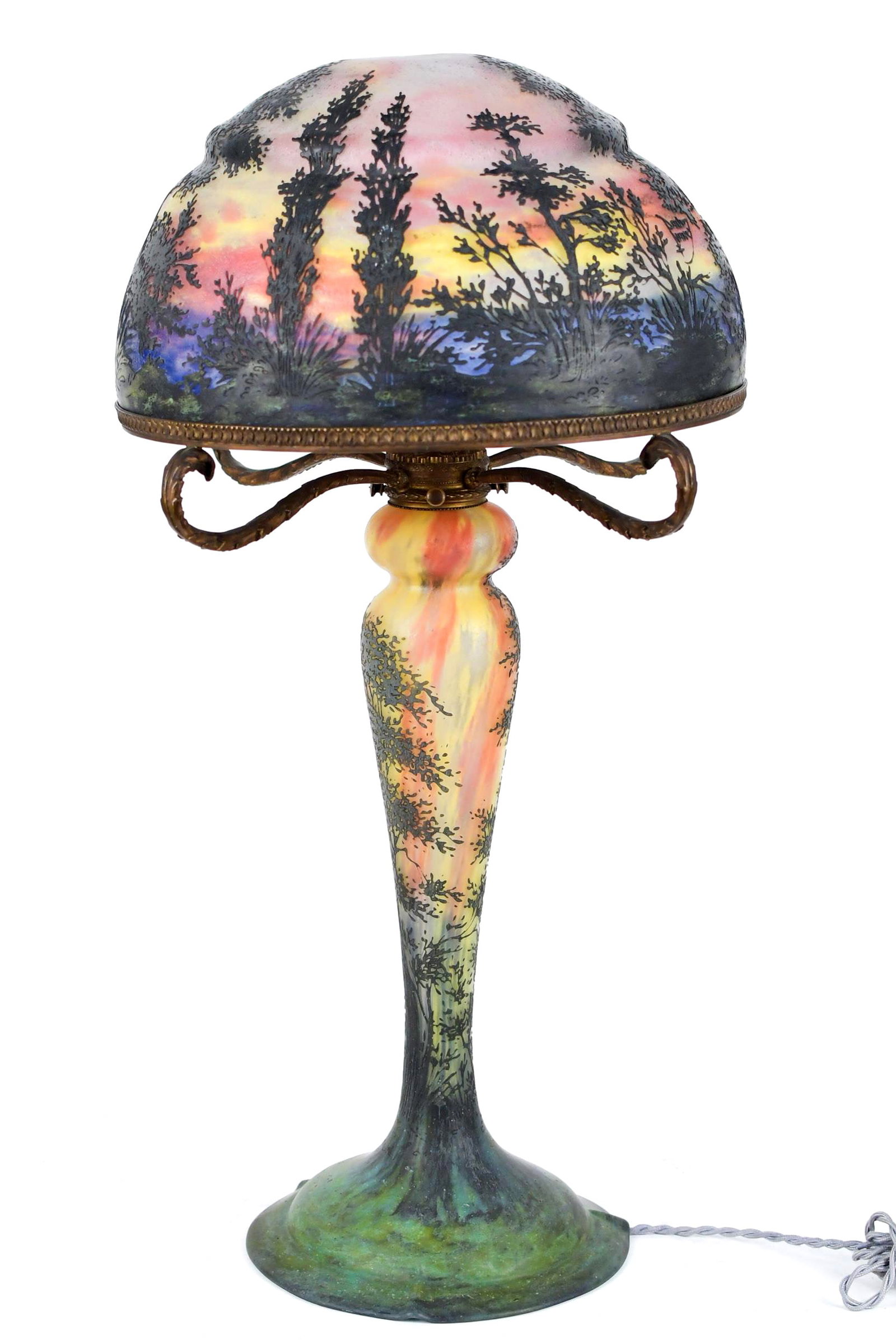 FINE DAUM NANCY SUNSET CAMEO GLASS LAMP.: A signed Daum Nancy Sunset cameo glass table lamp, internally decorated with sunset landscape overlooking lake, on a tree form base. Shade signed Daum Nancy with Crois de Lorraine, four cast bronze su