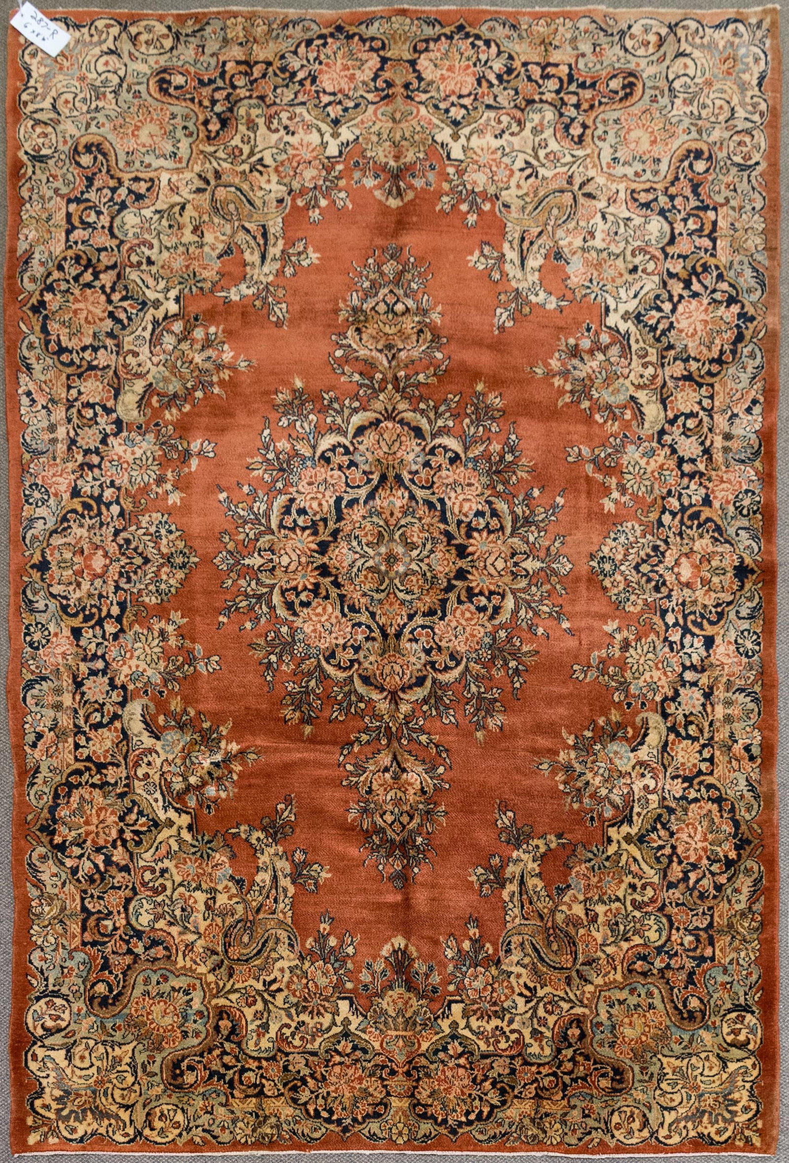 ANTIQUE PERSIAN KERMIN ORIENTAL RUG.: An antique hand woven Persian Kirman Oriental area rug with a brick red ground, highlighted with tan and cobalt blue.6' x 8'10”.
