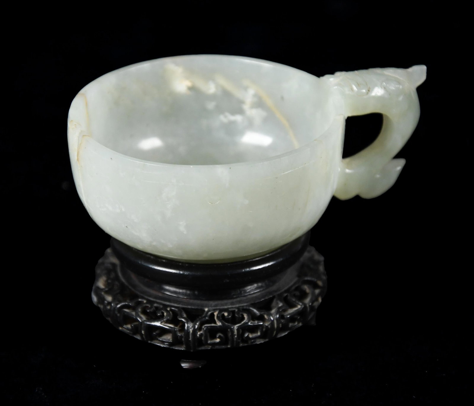 ANTIQUE CHINESE CARVED CELADON JADE TEA CUP.: A small antique Chinese carved celadon jade tea cup with a dragon formed handle and separate wooden base. Tea cup 3.75”W, Overall on stand 2.5”H. Provenance: from a private CT collection.