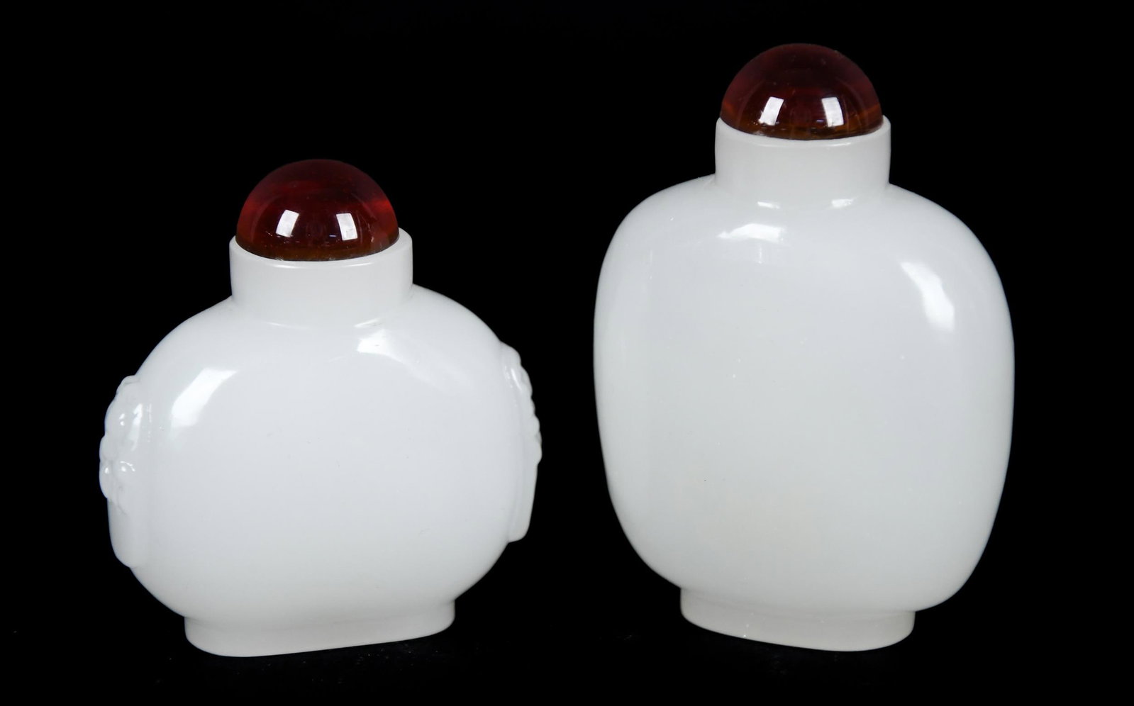 TWO CHINESE WHITE JADE SNUFF BOTTLES.: Two similar Chinese white jade snuff bottles, with colored stoppers, smaller with carved details on sides, 2.5” and 3.25”H.