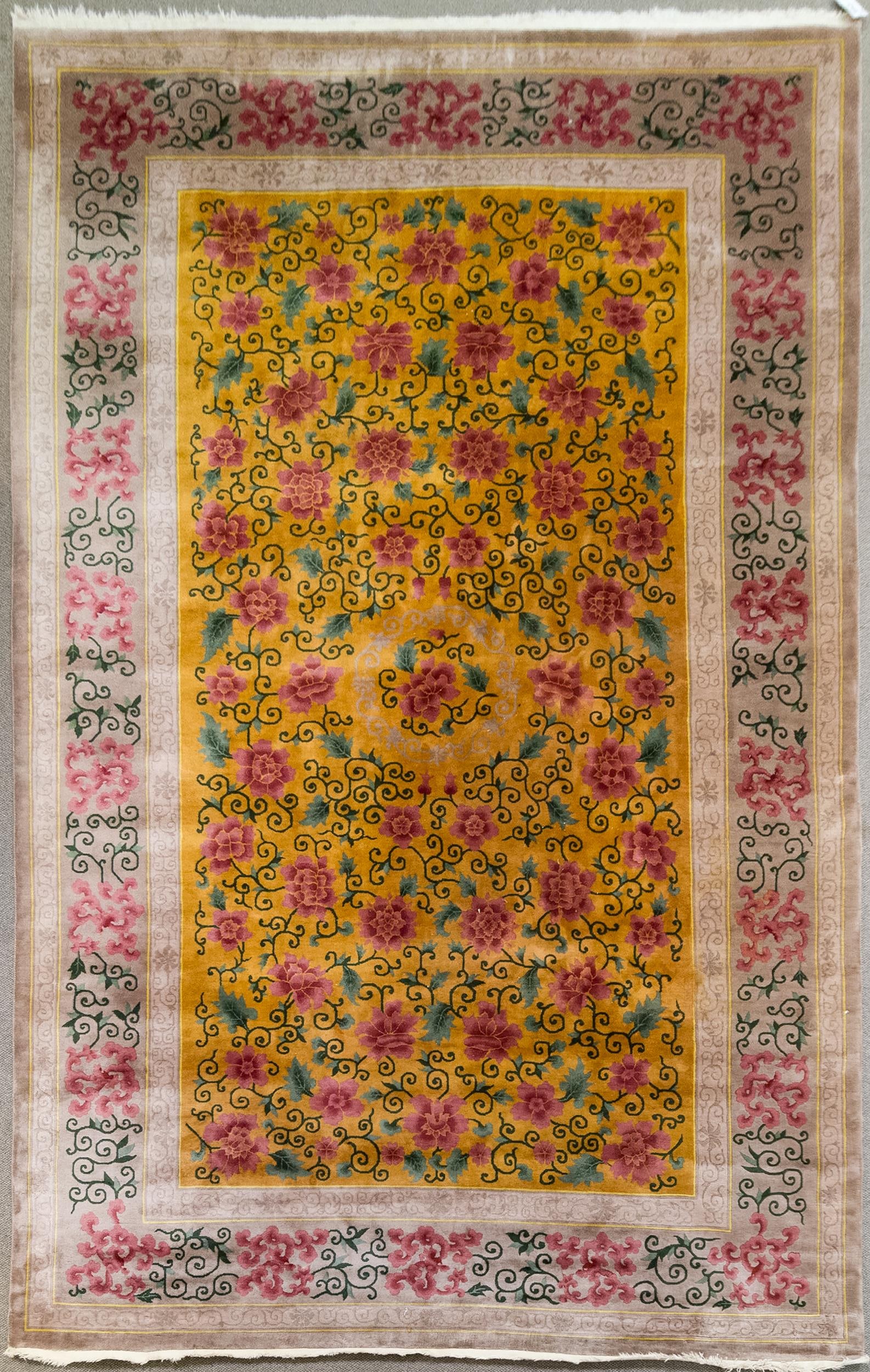 VINTAGE NICHOLS CHINESE ROOM SIZE RUG.: A vintage Nichols Chinese room size rug with gold ground, highlighted with stylized floral blossoms and vines in pick and green. 9’8” x 15’4”.