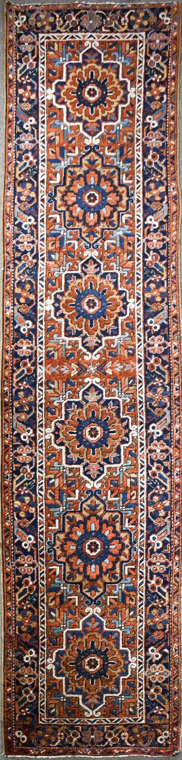 ANTIQUE HERIZ HALL RUNNER.: An antique hand woven Oriental Heriz hall runner rug with a red ground, highlighted with blues, tan, and ivory.2’11” x 11’6”.