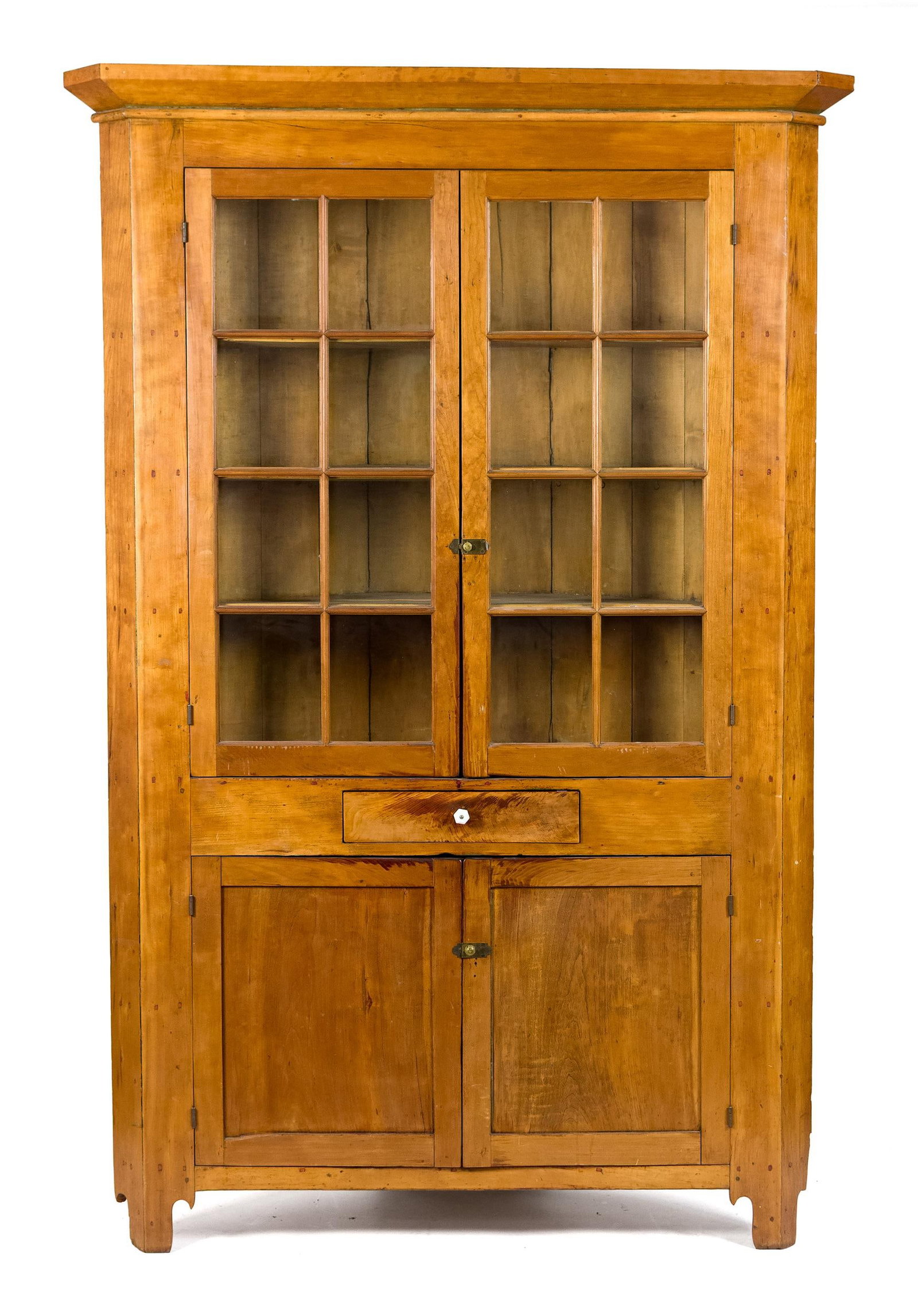19TH C. AMERICAN CHERRY CORNER CUPBOARD.: A ca. 1820 American single part cherry corner cupboard with an applied cornice molding over two, eight light glass doors, over a single drawer in front frieze and two lower paneled doors below.