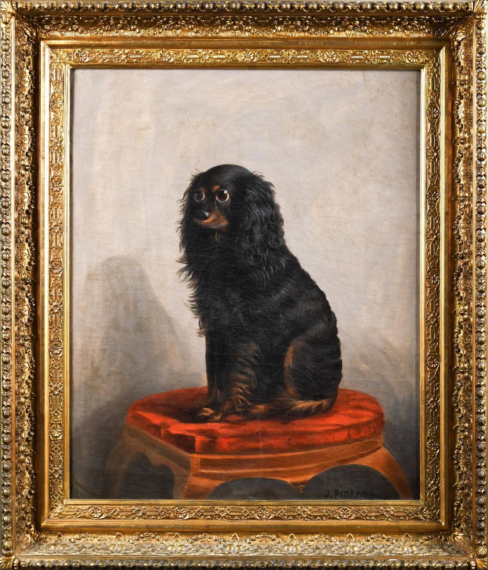 19TH C. J. PINKNEY OIL, DOG ON STOOL.: A 19th C. oil on canvas, small black dog with large eyes on a stool with red cushion, signed lower right J. Pinkney 1857. Canvas 27.5” x 22”, Frame 34” x 39”.