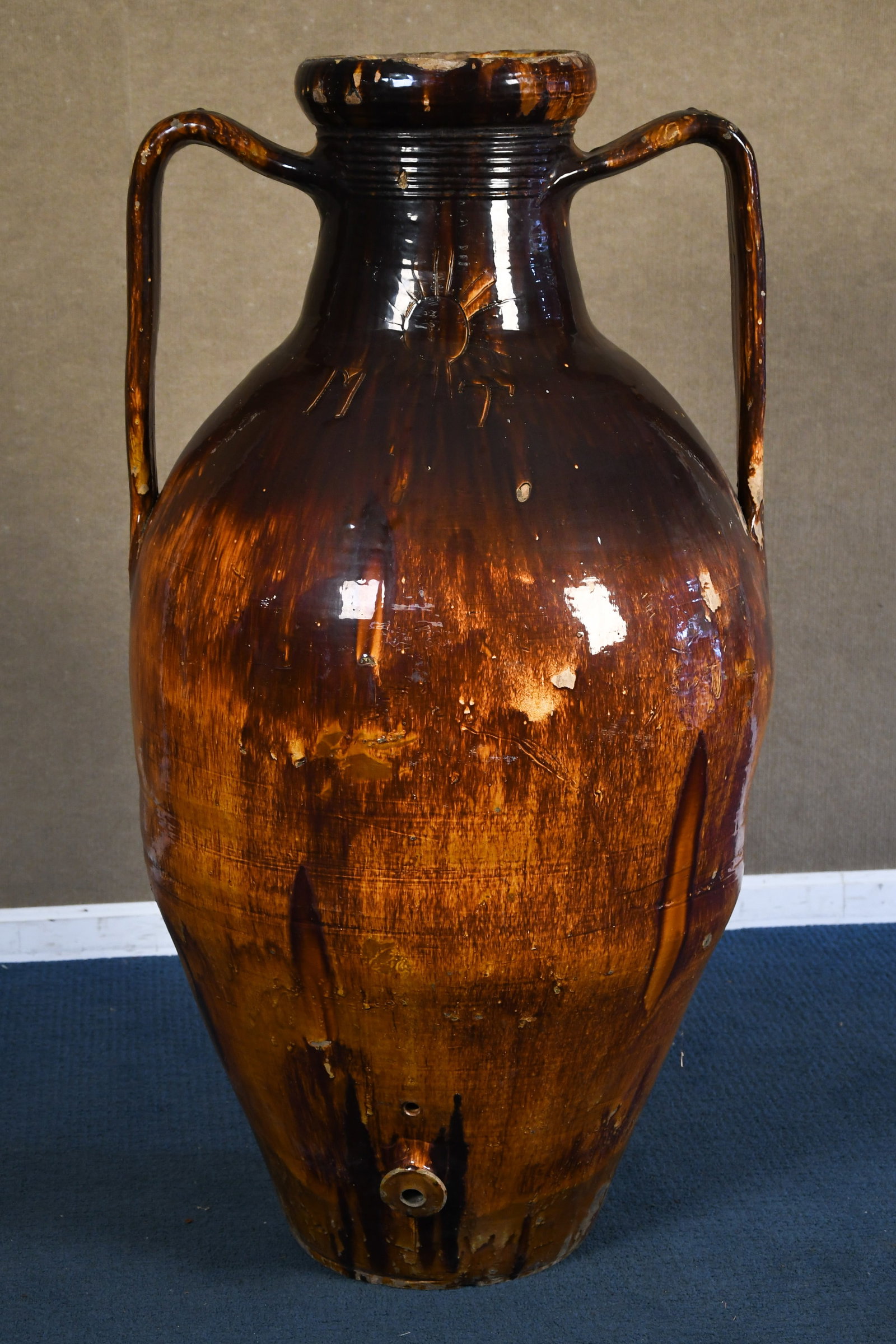 ANTIQUE ITALIAN OLIVE OIL AMPHORA (1 OF 3).: A large antique Italian terracotta double handled olive oil amphora, in brown glaze, spigot at bottom, engraved at shoulder MT, with sun. 52”H x 27”W.