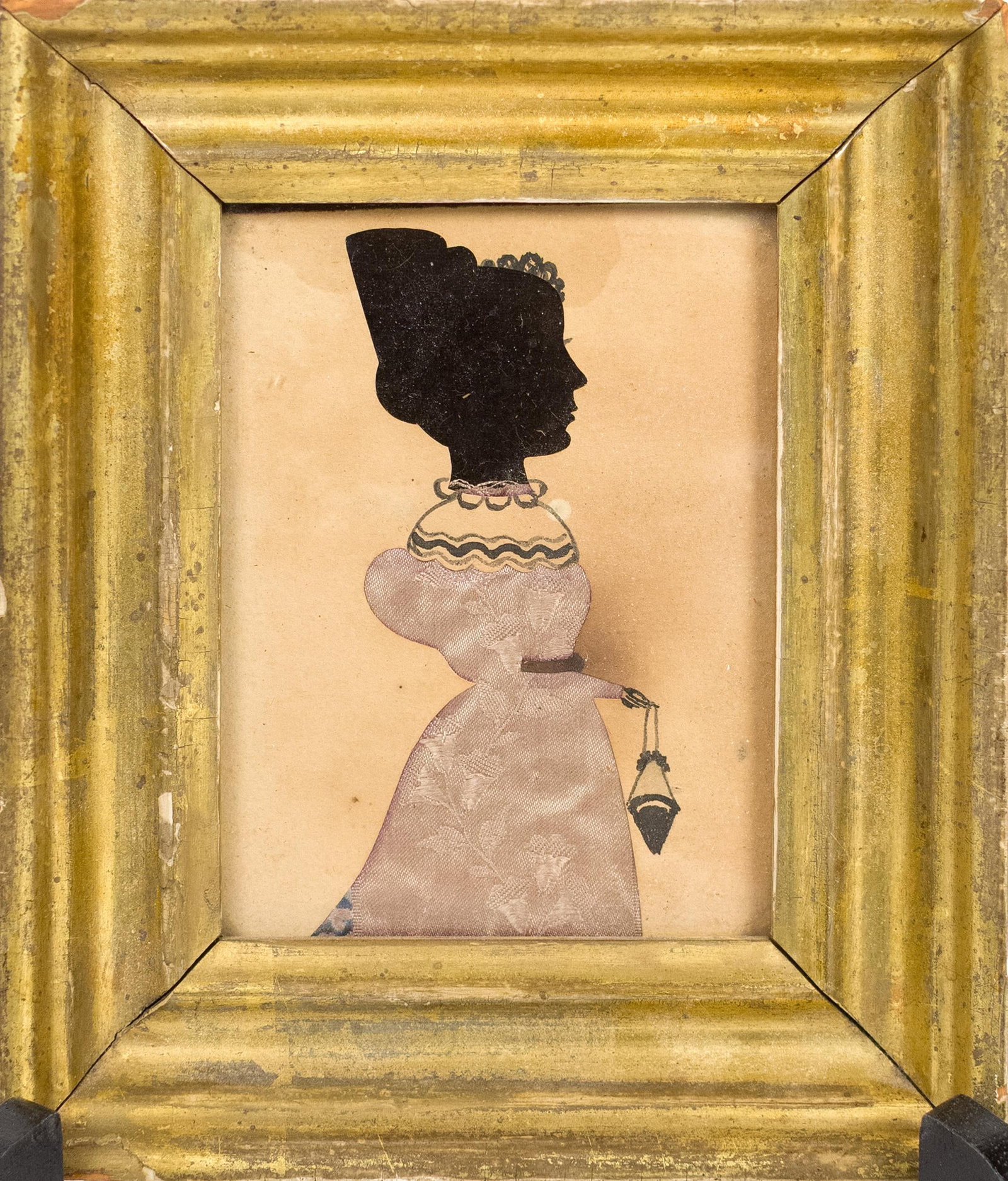 19TH C. HAND COLORED HOLLOW CUT SILHOUETTE.: A 19th C. American school hollow cut silhouette with hand coloring depicting, a young woman in a blue gray fabric dress holding a purse, in a period lemon gold frame. Image 4” x 3”, Frame