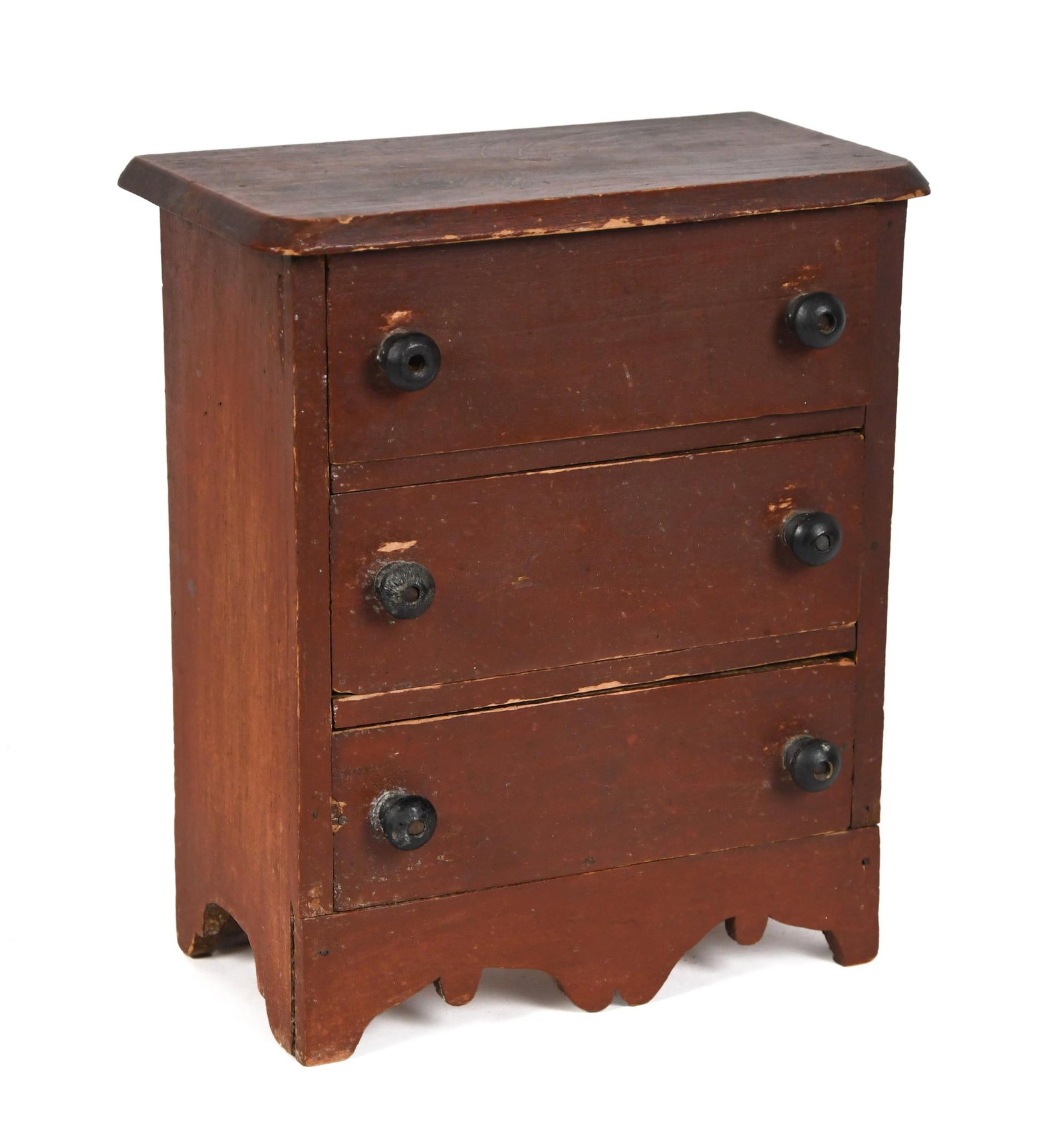 19TH C. RED PAINTED CHILDS CHEST.: A mid 19th C. child size 3 drawer chest with original red paint and black painted wood knobs, with a nicely scrolled apron 11.5“H x 9.5“W x 5“D. Provenance: from the lifelong,