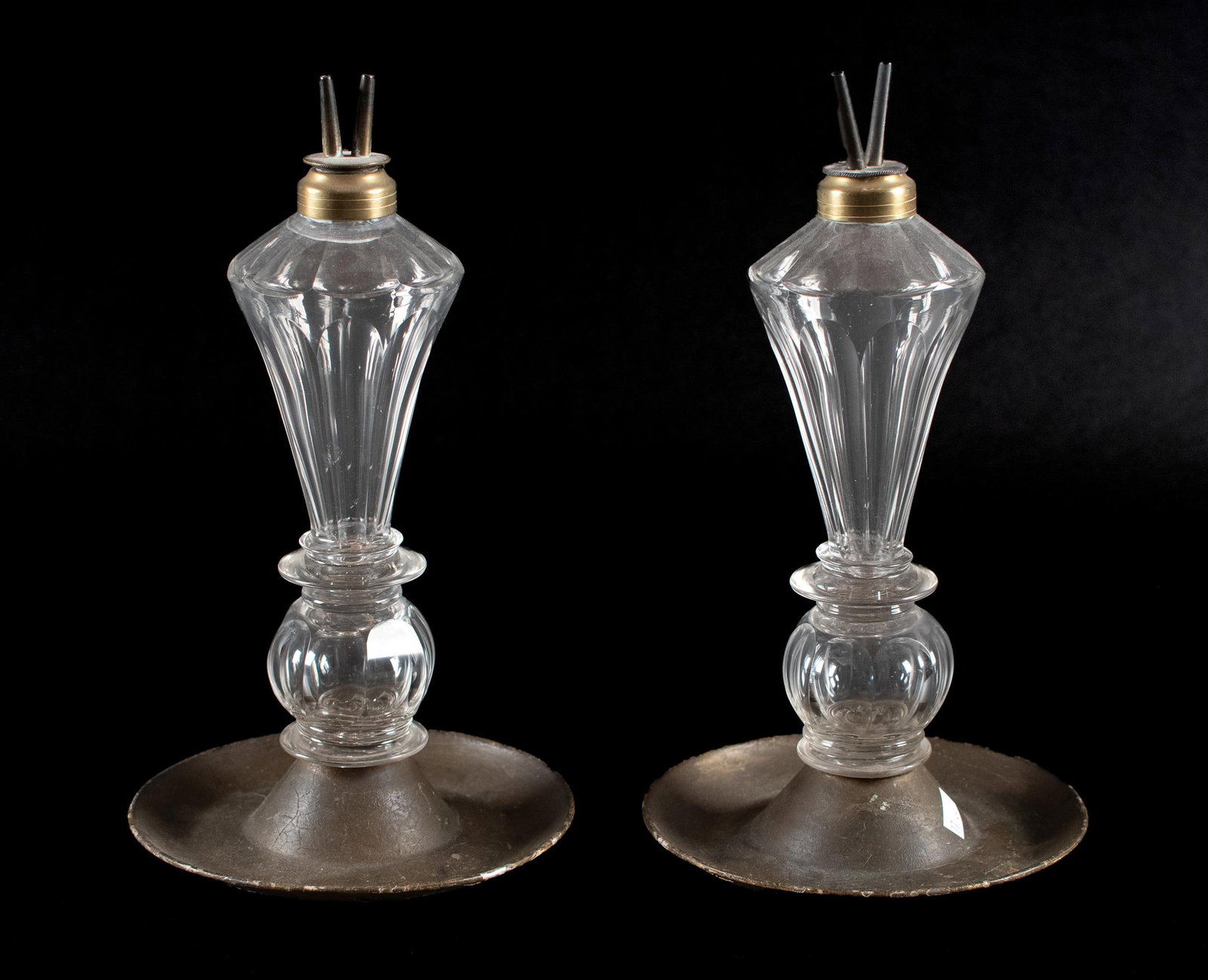 PR. RARE 19TH C. SANDWICH WHALE OIL LAMPS WITH TIN.: Pair of rare 19th C. Sandwich glass whale oil lamps with tin bases, ribbed clear glass font on a pressed-glass base with copper collar. 11.75”H x 6.5” dia. base. See label on underside of 