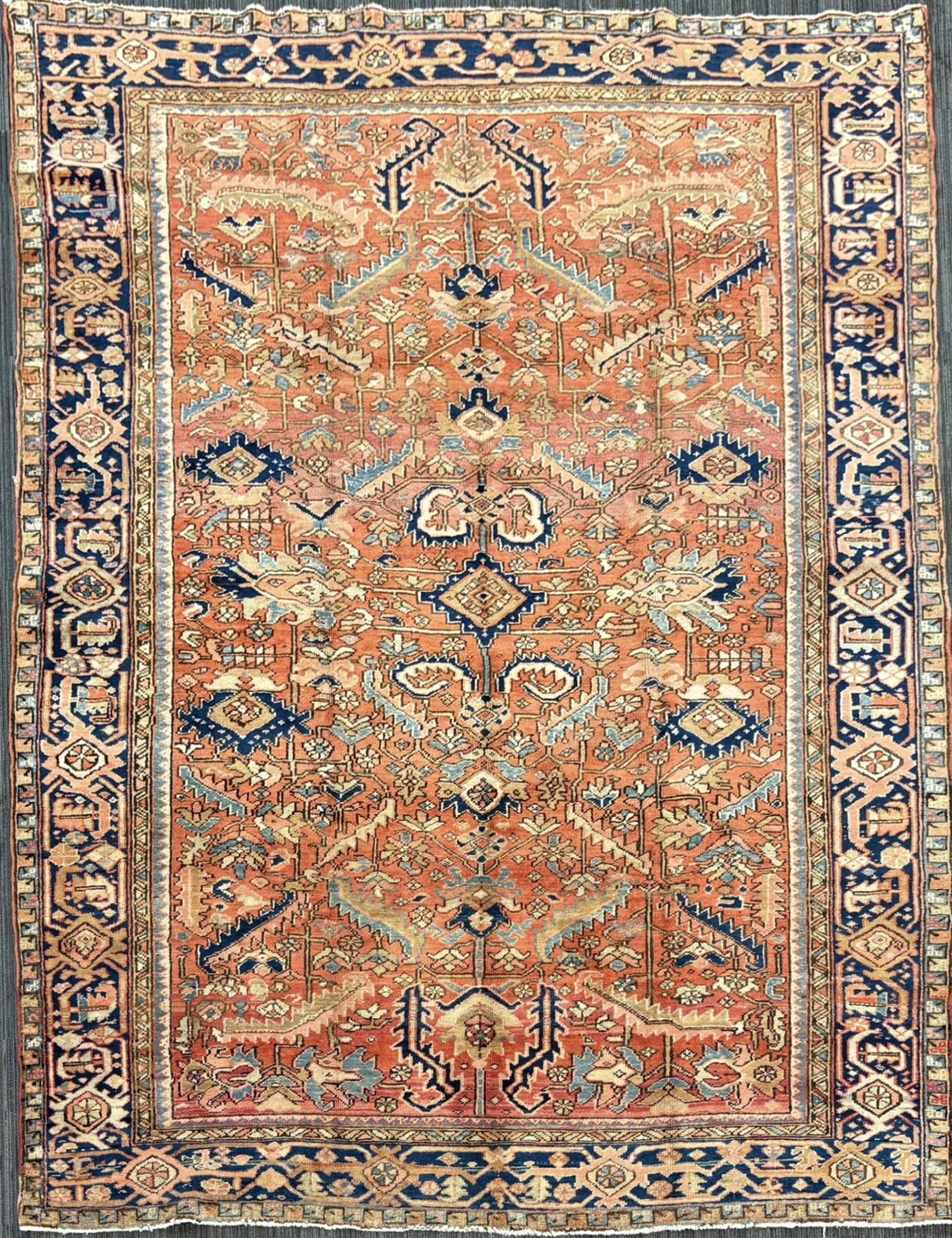 ANTIQUE ORIENTAL HERIZ RUG.: An antique Oriental Heriz rug with a rust red field densely decorated with an allover floral design of palmettes, rosettes, scrolling vines, and leafy sprays in ivory, navy, pale blue, sage, and muted
