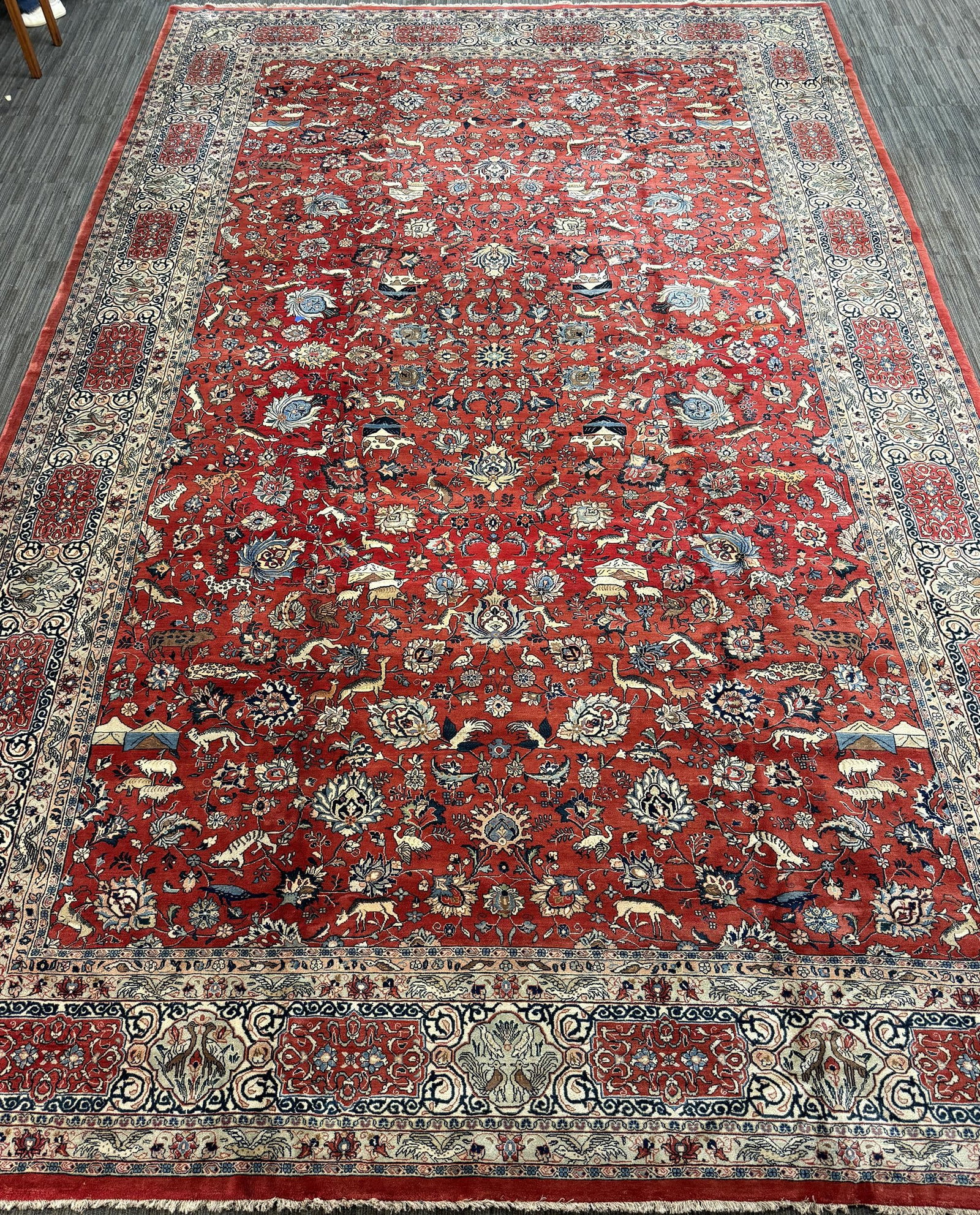 VINTAGE ORIENTAL PALACE SIZE PICTORIAL RUG.: A vintage Oriental palace size rug, with a coral-red field densely decorated with an allover pattern of flowering vines, palmettes, rosettes, with wild animals and hunting tents, in ivory, pale blue,