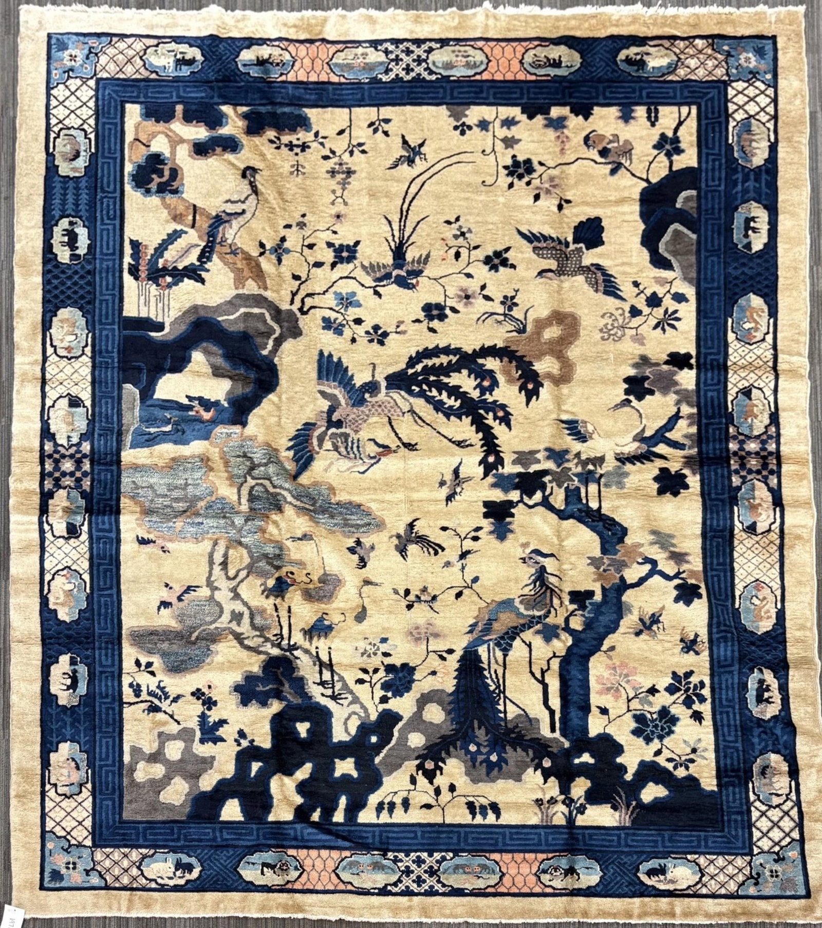 ANTIQUE CHINESE PICTORIAL ROOM SIZE RUG.: An antique Chinese pictorial carpet, decorated with a lively landscape scene of dragons, birds, flowering branches, cloud forms, and stylized rockwork in shades of blue, pale pink, tan, and brown on