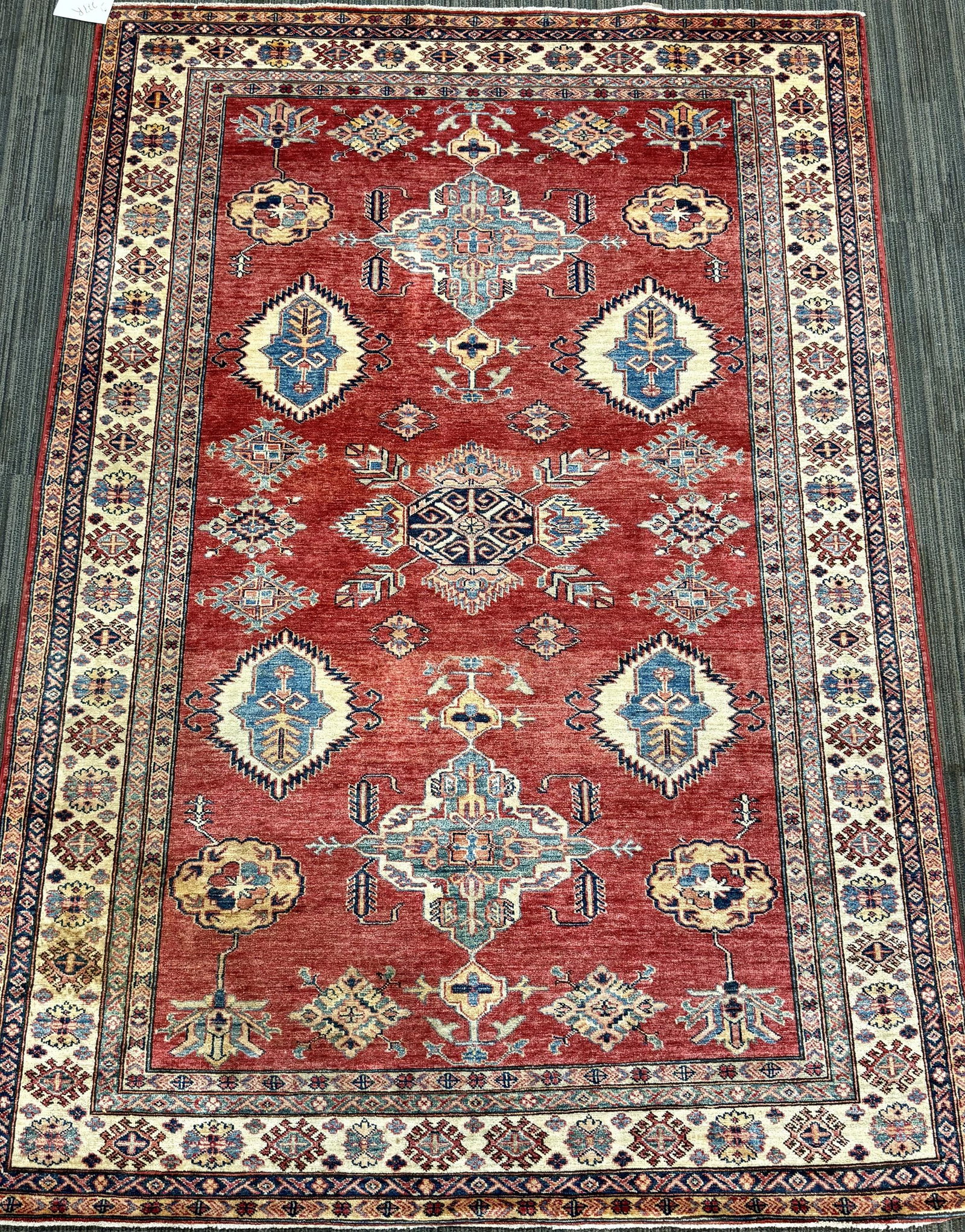 VINTAGE ORIENTAL ROOM SIZE RUG.: A hand-knotted Caucasian-style area rug, with a warm brick-red field centered by a series of geometric medallions and stylized tribal motifs in ivory, blue, gold, and green. Multiple borders