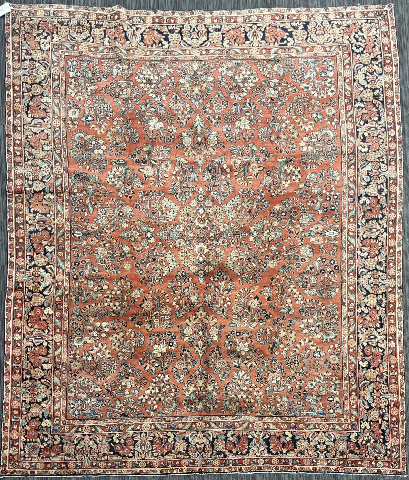 ANTIQUE ORIENTAL SAROUK RUG.: An antique Persian Sarouk carpet with a red field densely decorated with an allover floral design of palmettes, rosettes, scrolling vines, and leafy sprays in ivory, navy, pale blue, sage, and muted g
