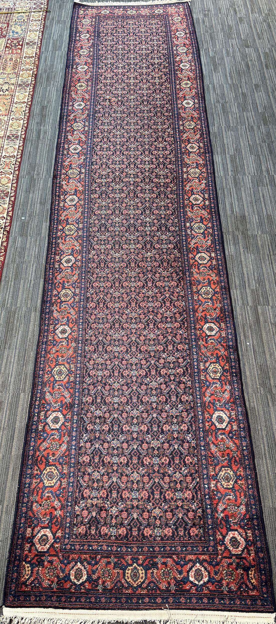 VINTAGE ORIENTAL RUNNER RUG.: A vintage Oriental runner, with a dark navy field densely patterned with repeating small boteh and floral motifs in rust, blue, ivory, and muted red. Surrounded by a broad rust-red border of repeating
