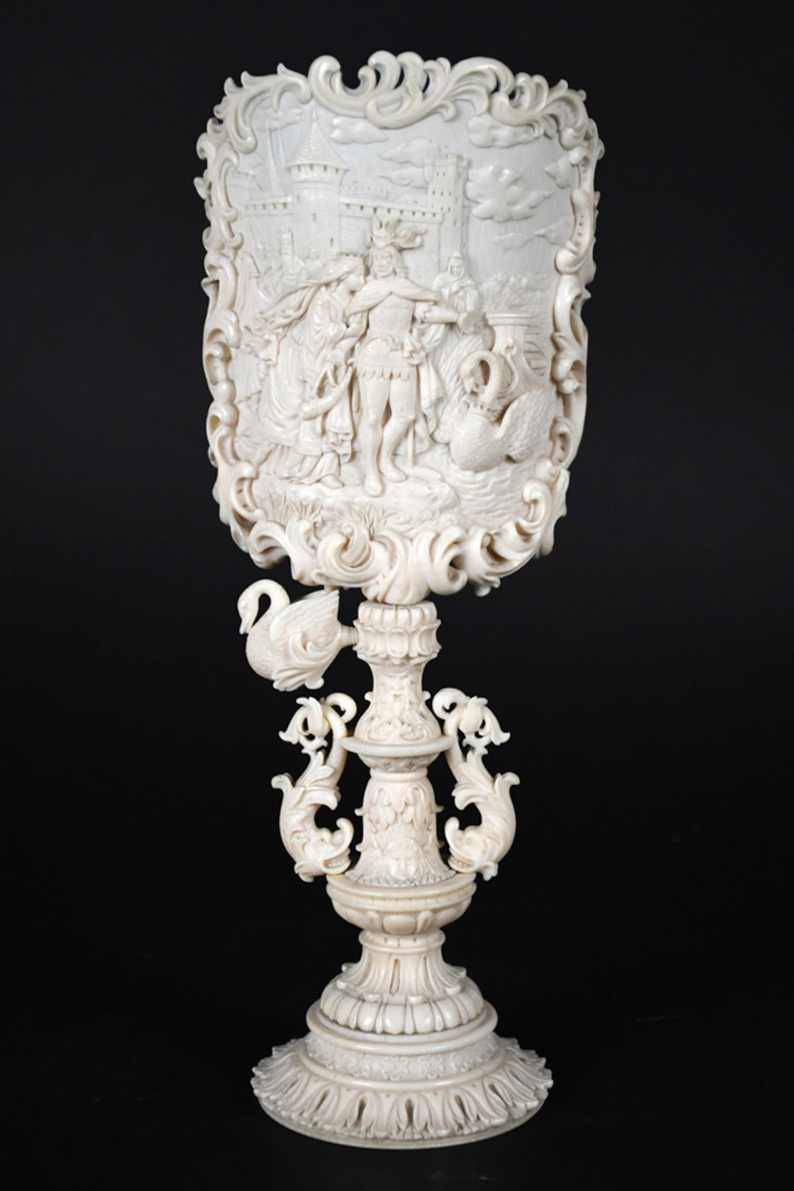 ANTIQUE EUROPEAN CARVED BONE CANDLE SCREEN.: An antique European elaborately carved bone table candle screen with large shaped panel depicting a medieval courtly scene before a castle, surrounded by pierced scrolling foliate ornament. Supported 