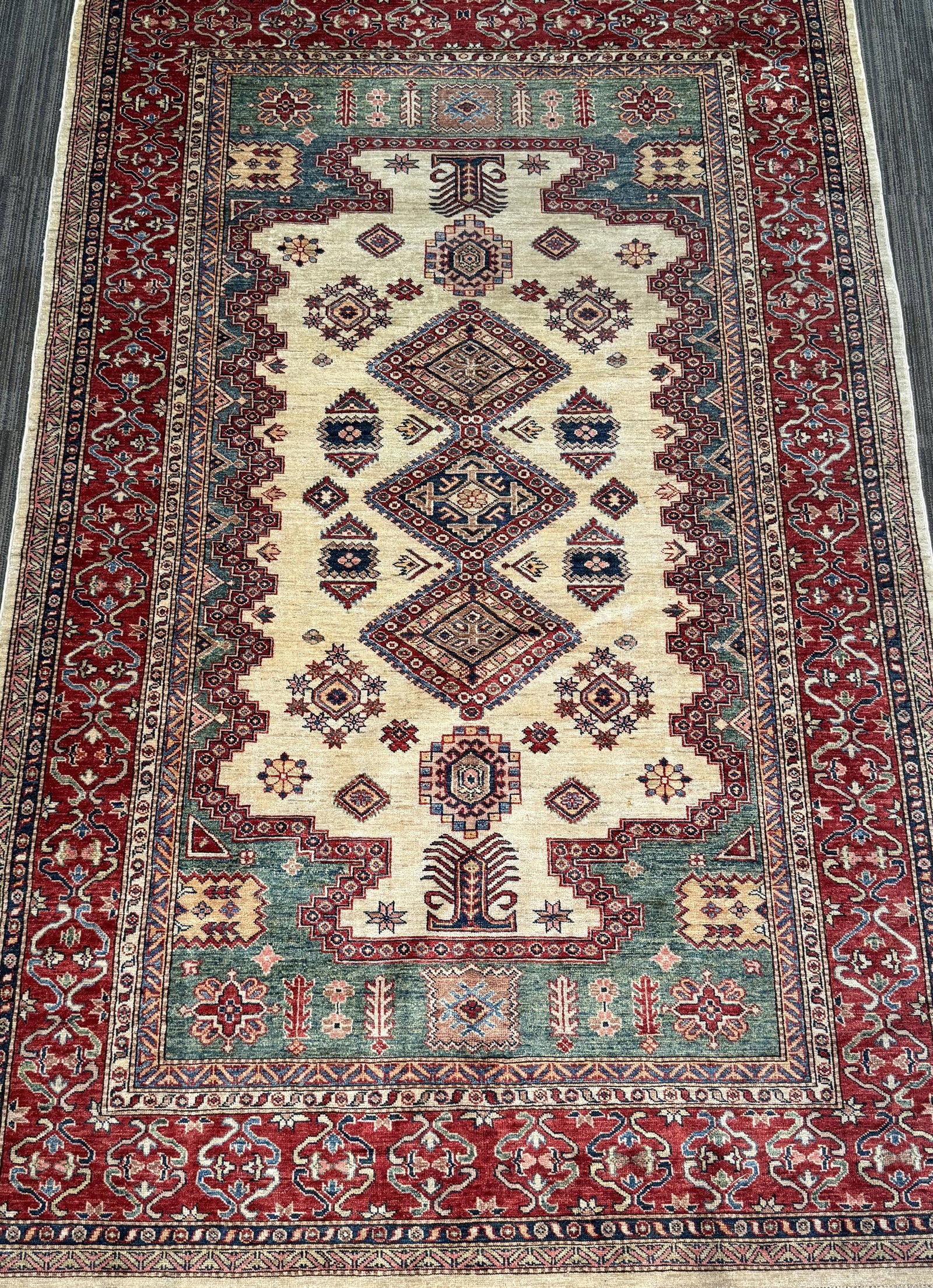 VINTAGE ORIENTAL AREA RUG.: Vintage Oriental are rug, with ivory field centered by a vertical arrangement of geometric diamond medallions and stylized floral motifs in rose, blue, green, and burgundy. With red borders. 5’9