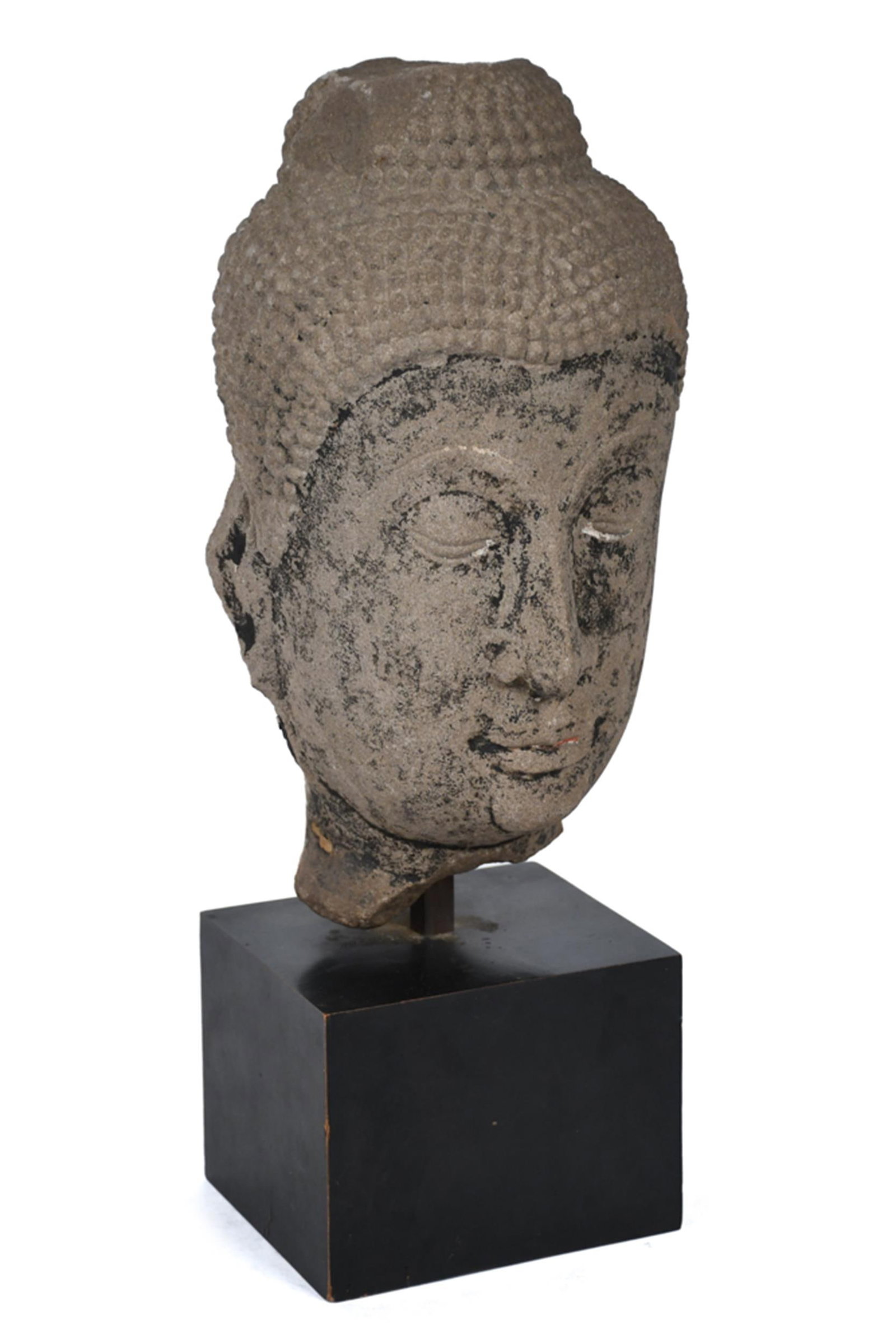 THAI AYUTTHAYA PERIOD SANDSTONE HEAD OF BUDDHA.: A Thai Ayutthaya Period carved sandstone head of the Buddha with serene downcast expression, elongated earlobes, tightly curled hair, retaining traces of dark surface coloration. Mounted on a later
