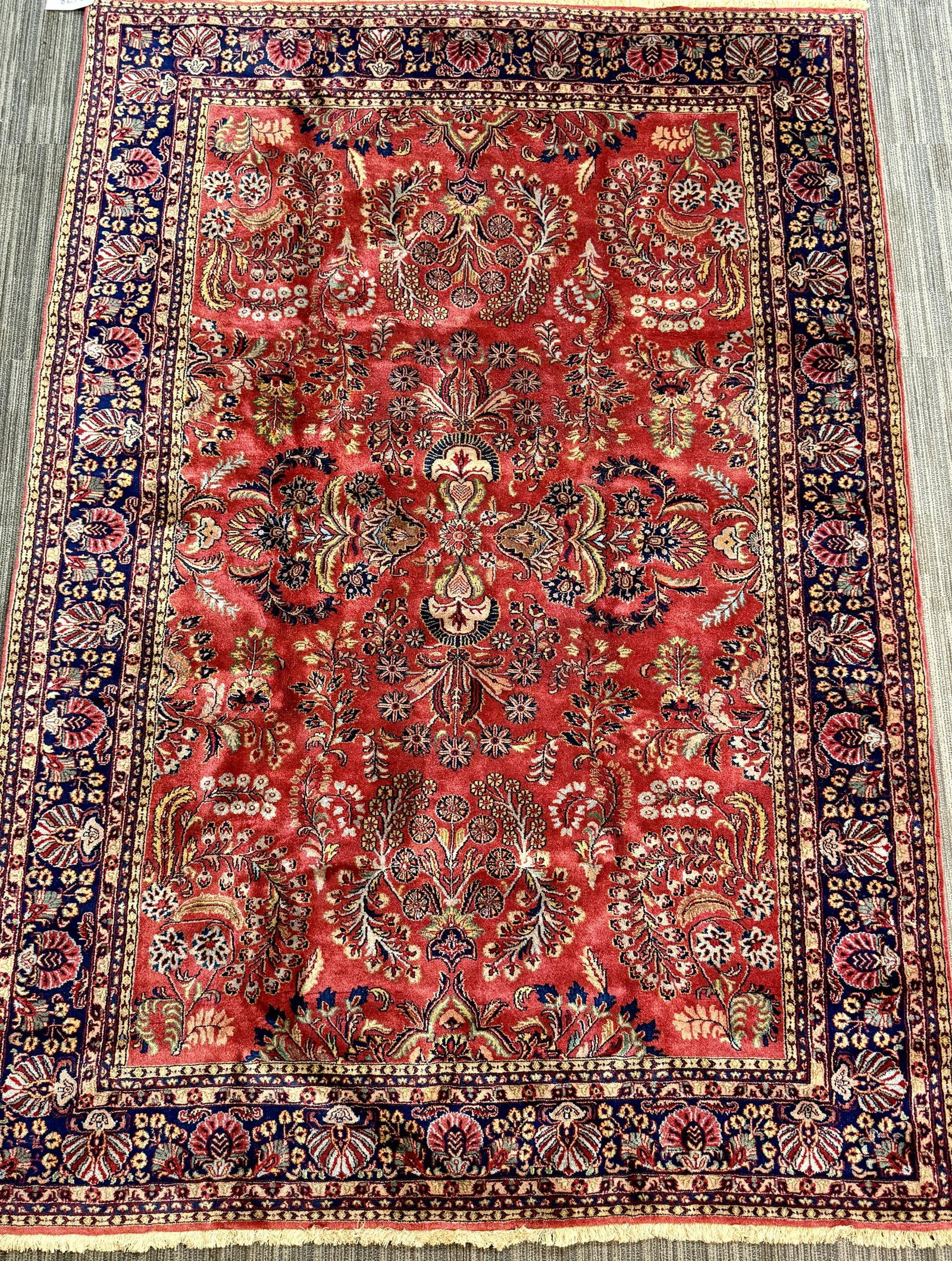 ANTIQUE ORIENTAL SAROUK RUG.: An antique Persian Sarouk carpet with a rich red field densely decorated with an allover floral design of large scrolling palmettes, blossoms, and leafy vines in navy, ivory, blue, and muted green. Su
