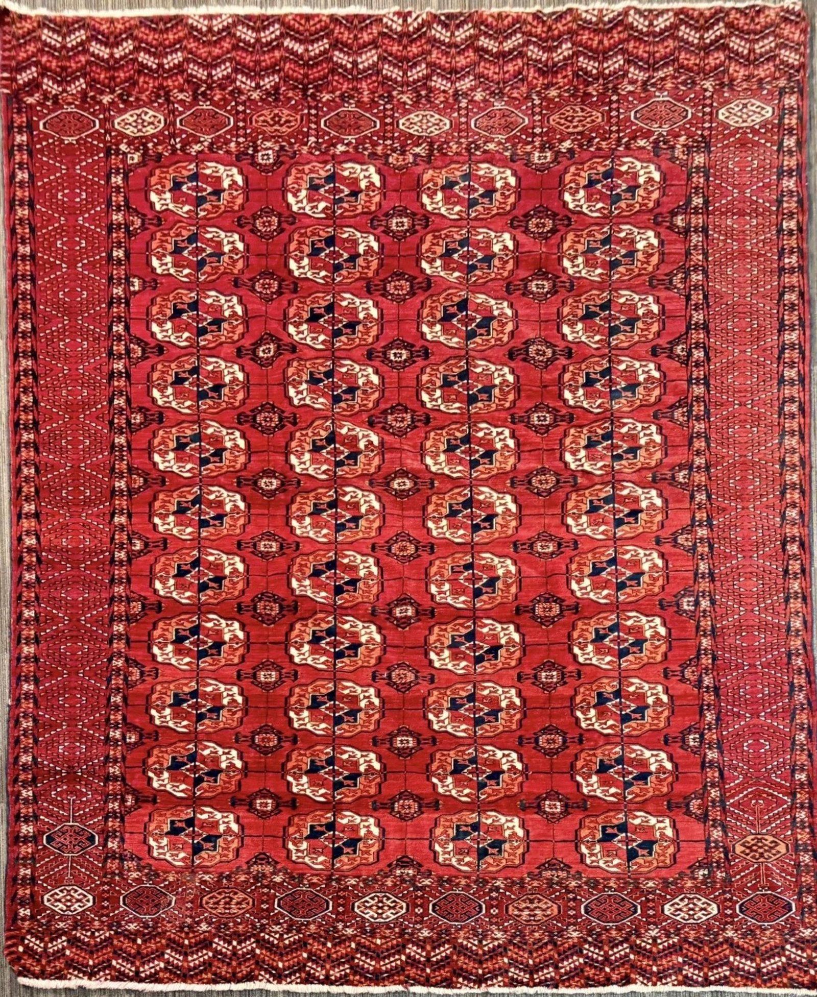 ANTIQUE ORIENTAL TEKKE RUG.: Antique Oriental Tekke carpet, with a deep red field arranged in repeating rows of octagonal medallions in ivory, rust, dark brown, and black, enclosed by multiple geometric borders. 7’6” 