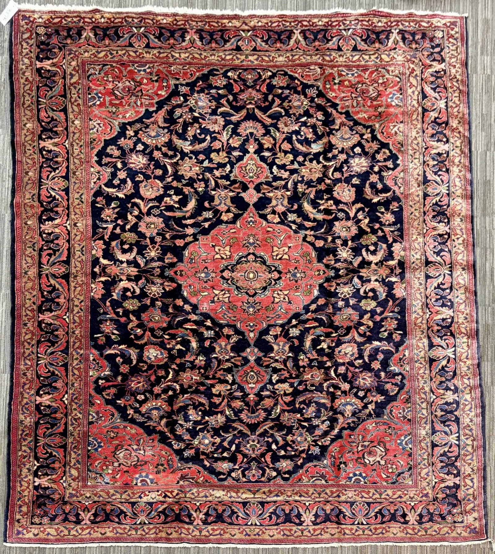 VINTAGE ORIENTAL ROOM SIZE RUG.: A vintage Oriental room size rug, with a deep navy field centered by a large salmon-red floral medallion and densely decorated with scrolling vines, palmettes, blossoms, and leafy sprays in rose, ivor