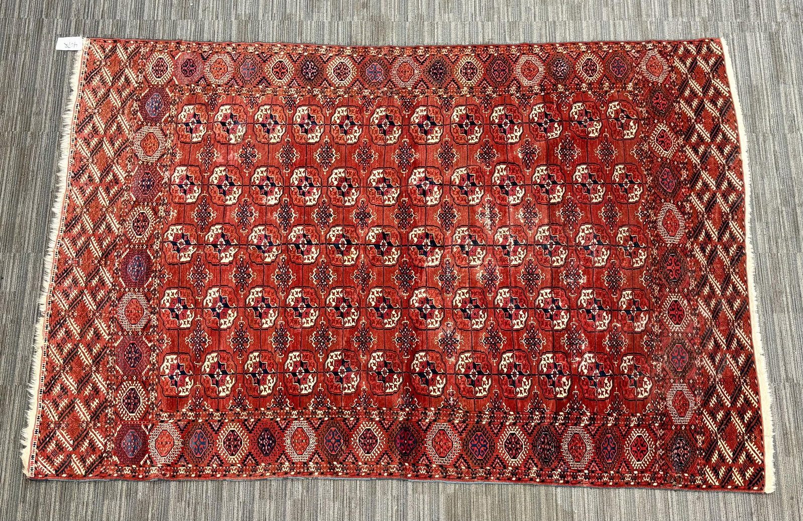 VINTAGE ORIENTAL BOKARA AREA RUG.: A vintage Bokara rug with a rich red field and repeating rows of traditional octagonal medallions alternating with smaller geometric motifs in ivory, dark blue, black, and red. The field is