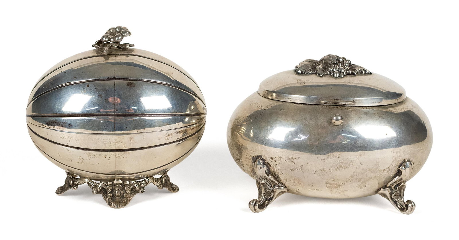 TWO JUDIACA SILVER ETROG BOXES.: Two Judiaca silver etrog boxes, each of oval bombe form with hinged cover and raised on decorative feet. One with a segmented body and domed cover surmounted by a small floral finial, raised on an