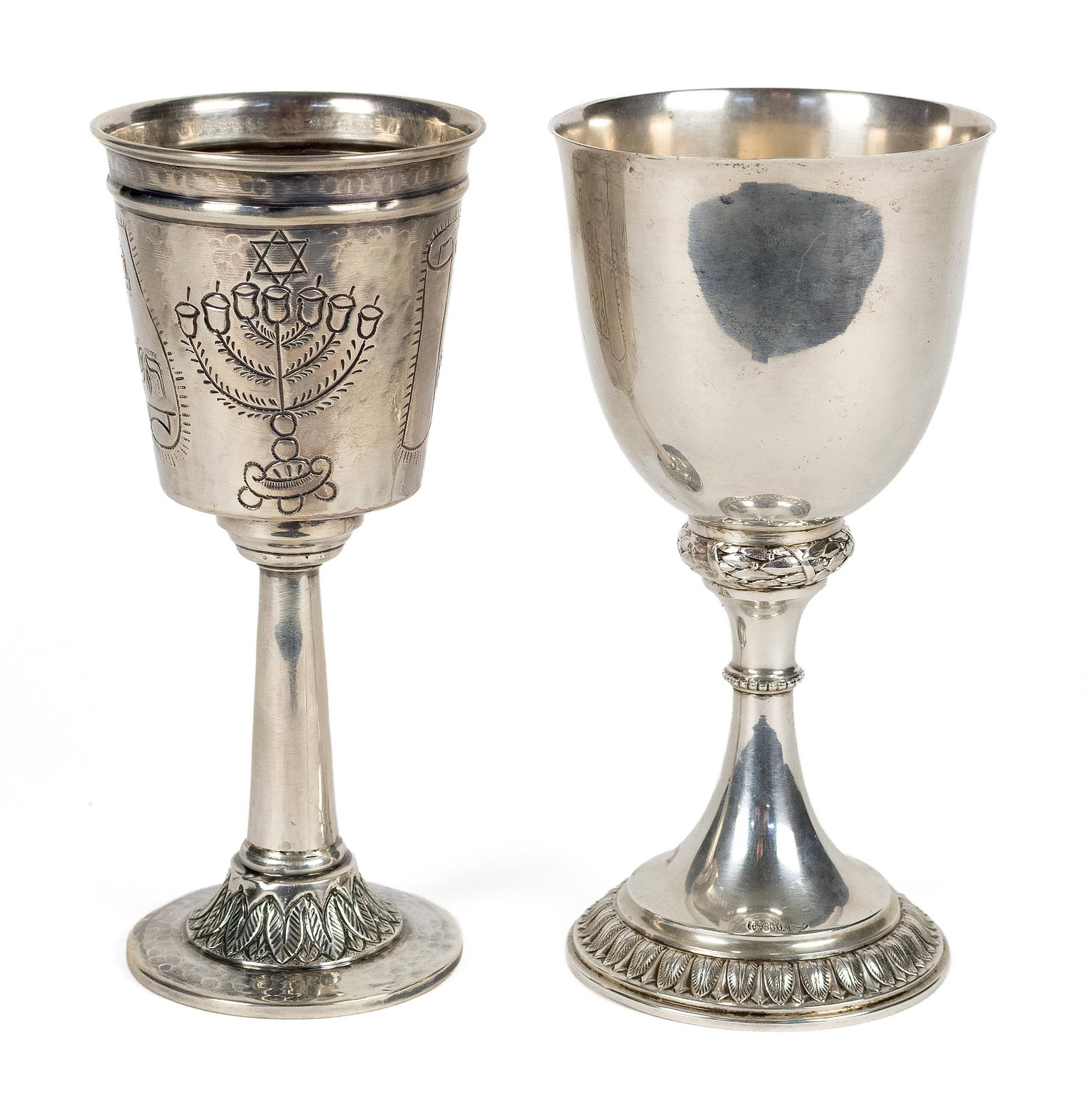 TWO SILVER KIDDUSH GOBLETS, MOSHE SMILOVICI.: Two silver Kiddush goblets, one with a plain polished bowl above a laurel wreath band, pedetal base with leaf decoration, stamped 800, 7.25”H. The other likely by Moshe Smilovici, with an engrav
