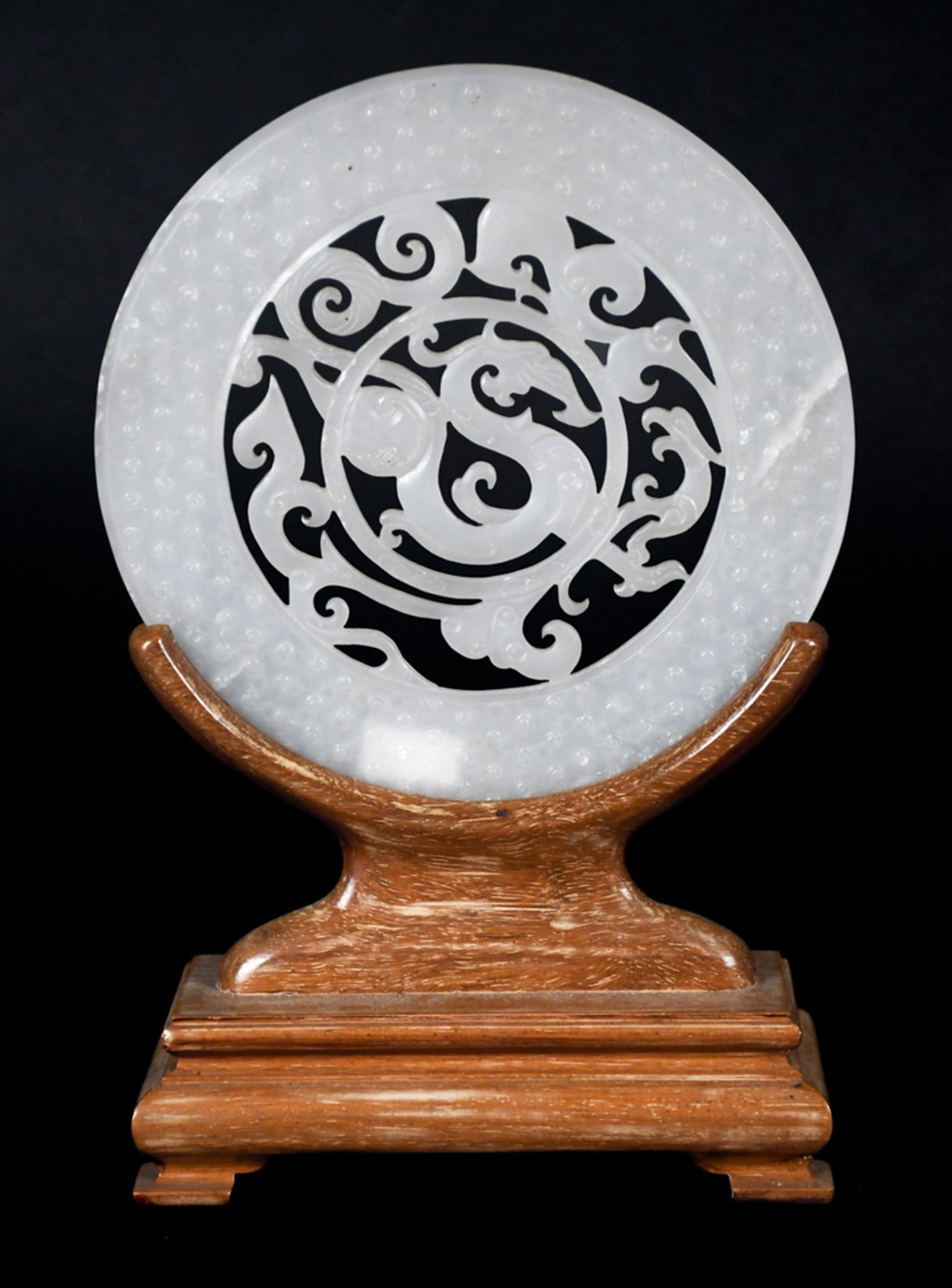 CHINESE WHITE JADE RETICULATED DRAGON DISC.: A 20th C. Chinese white jade reticulated disc on a fitted wood stand. The disc carved overall with small raised boss grain-pattern on the border, the pierced center depicting a sinuous dragon amid