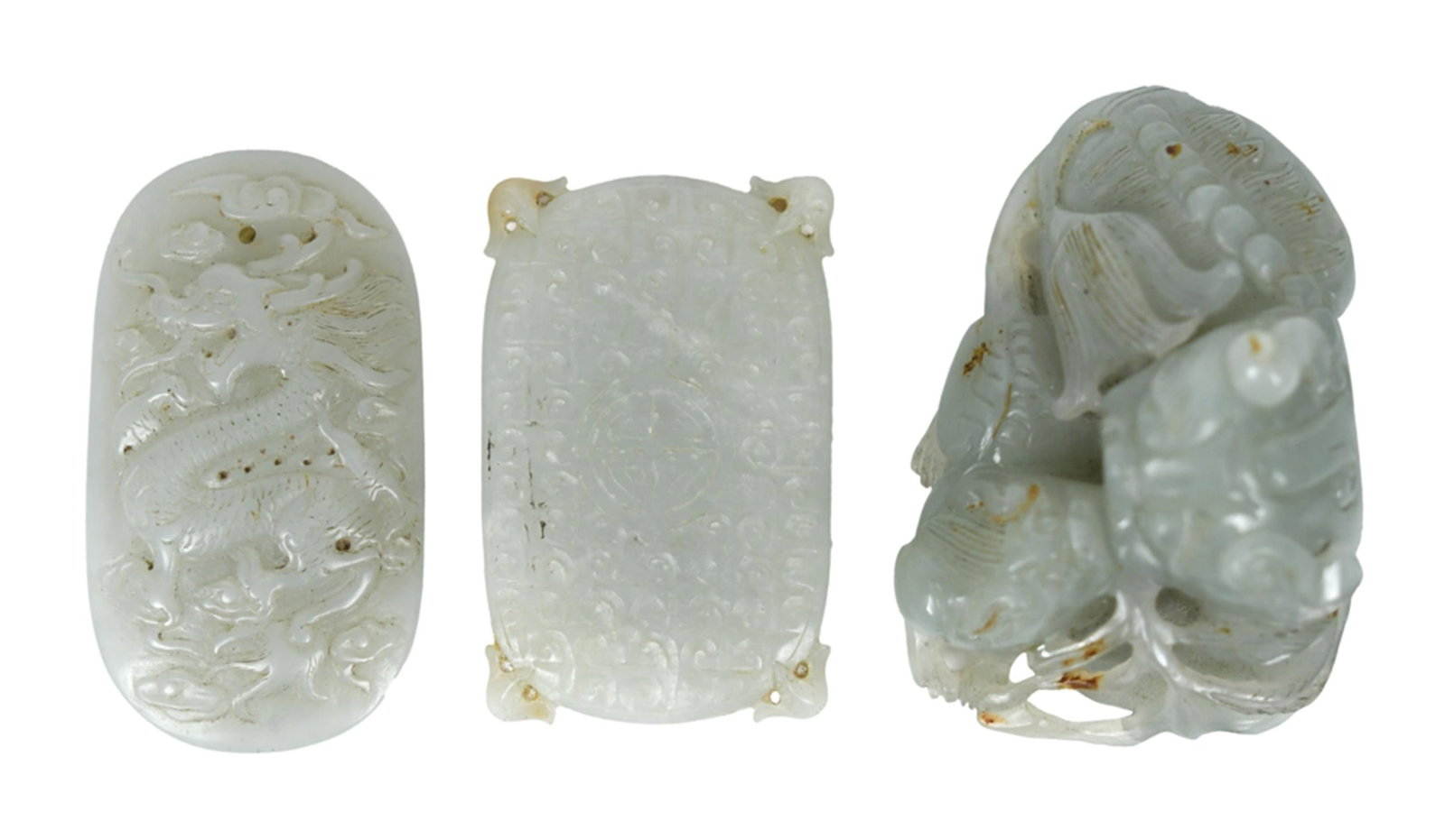 THREE CHINESE PALE CELADON JADE CARVINGS.: A collection of three Chinese pale celadon jade carvings, including:a dragon pendant, relief-carved with a dragon amid clouds, with suspension hole, 2.25”H;a recumbent foo lion group, carved in