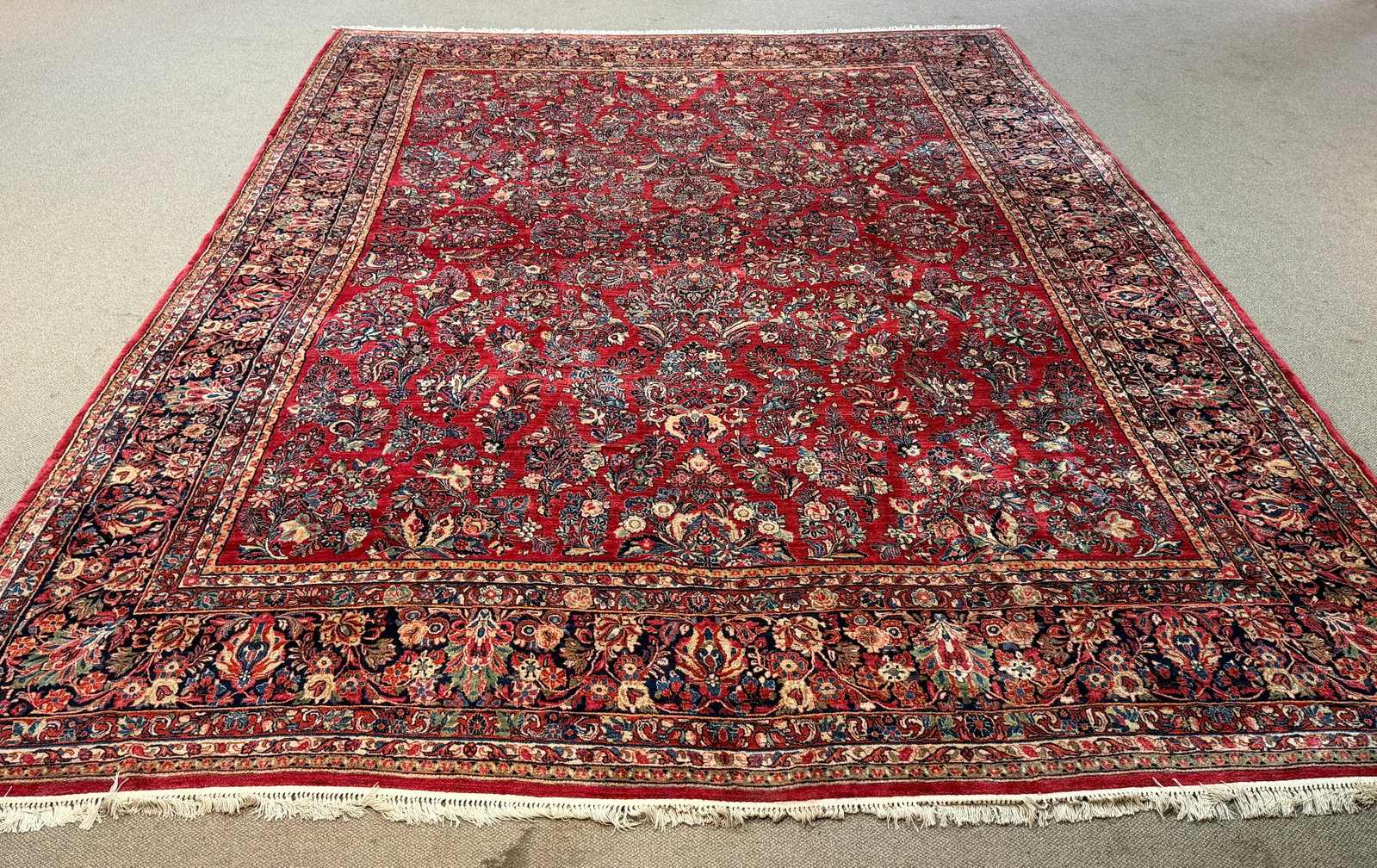 AN ANTIQUE PALACE SIZE ORIENTAL RUG.: A ca. 1920 palace size Persian Sarouk handmaid rug, with a red ground and blue, light green, and ivory floral pattern. 13’ 6” x 18’.