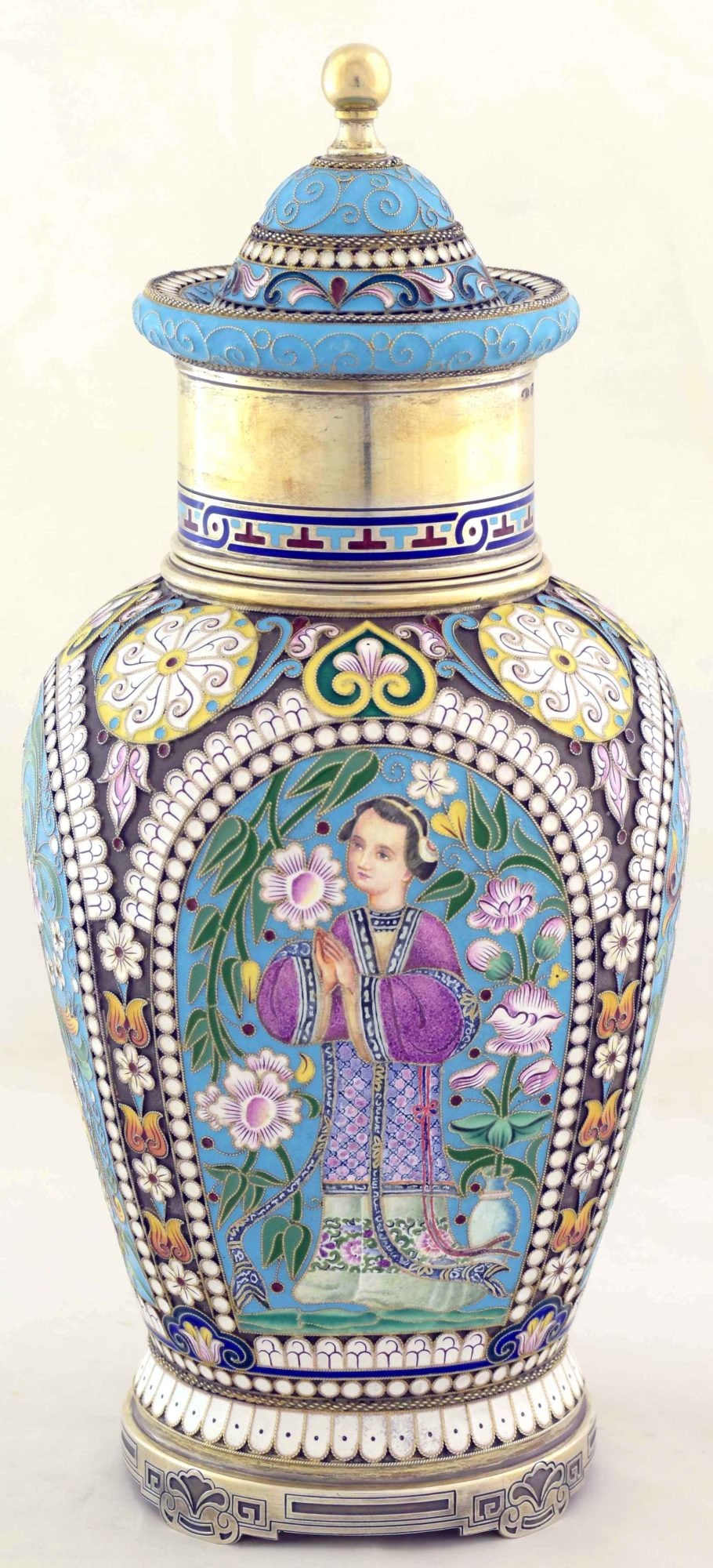 [Russian. Chinoiserie]. Silver tea-caddy depicting a young woman. - Russia, 20th century. - 21,5x9,5: [Russian. Chinoiserie]. Silver tea-caddy depicting a young woman. - Russia, 20th century. - 21,5x9,5 cm. Weight: 718 g. Silver; casting, multicolor enamels, gilding. Hallmarks: "Owchinnikow" (in Cyril