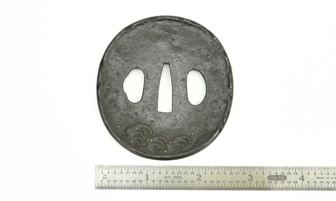 IRON TSUBA: Iron Tsuba Description: Iron Tsuba. Old figure with ornate robe standing on sword below figure. On the reverse are waves with gold and silver. Size: Length 3–3½ inches Accessories: None Acc