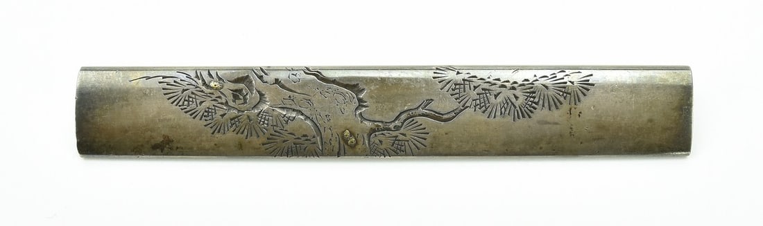 KINKO KODZUKA: Kinko Kodzuka Description: Kinko Kodzuka. Polished silver ground pine is deeply carved with gold accents. Pine needles are more lightly engraved. Dent is on reverse. Signed: Nomura Teru Masa.
