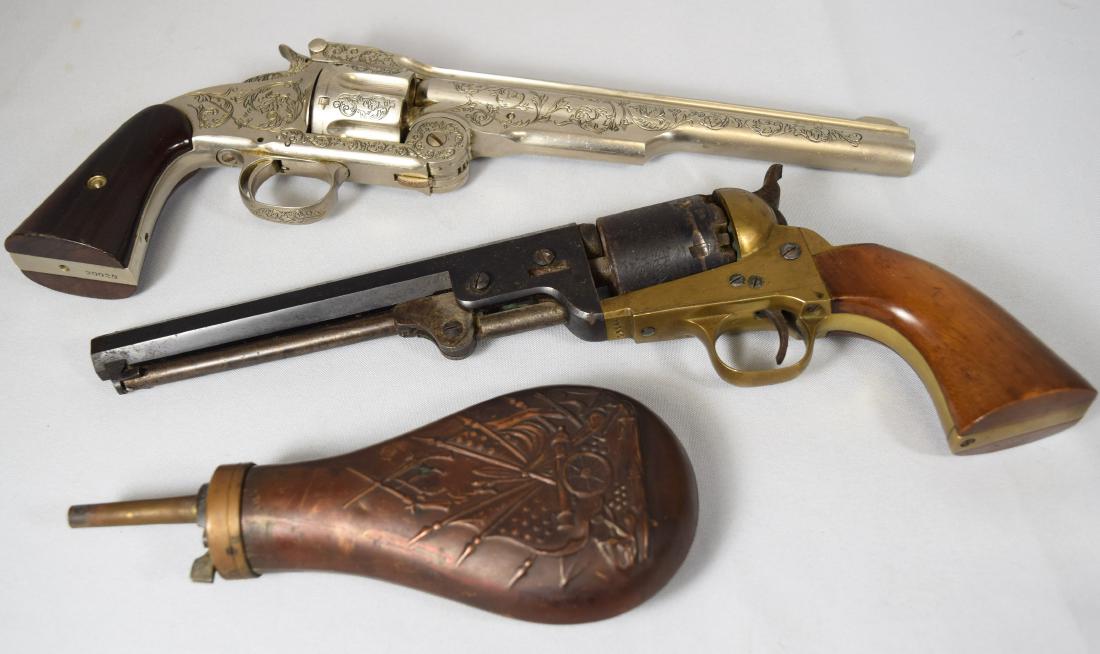 TWO BLACK POWDER REPLICA REVOLVERS & POWDER FLASK:: Three-piece grouping consisting of New Navy colt revolver by Euroarms, Italy. Bill Hitchcock nickel revolver (screw missing). Cannon and flag copper powder flask.
