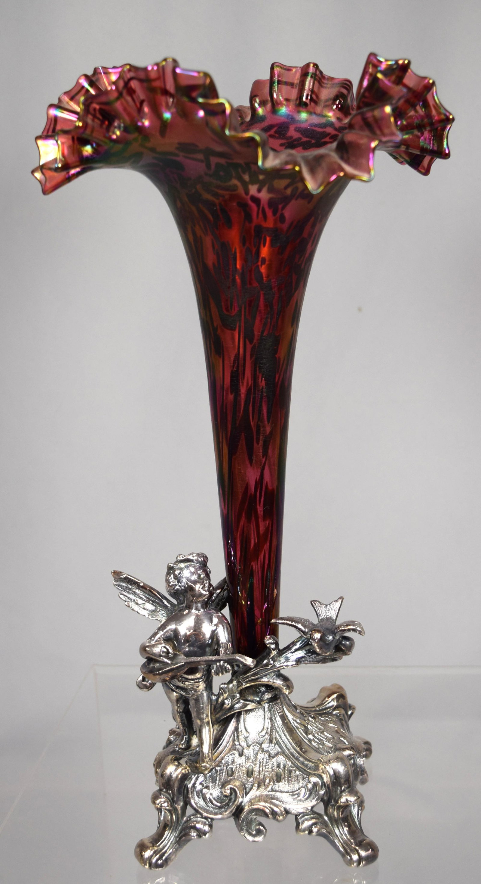 VICTORIAN SILVER PLATE & ART GLASS SINGLE: Measures 13 ¼ inches tall x 7 inches wide. Ruffle top trumpet shape art glass insert in iridescent deep cranberry colored glass with overall oil spot type decoration. Ornate figural footed 4-inch squ