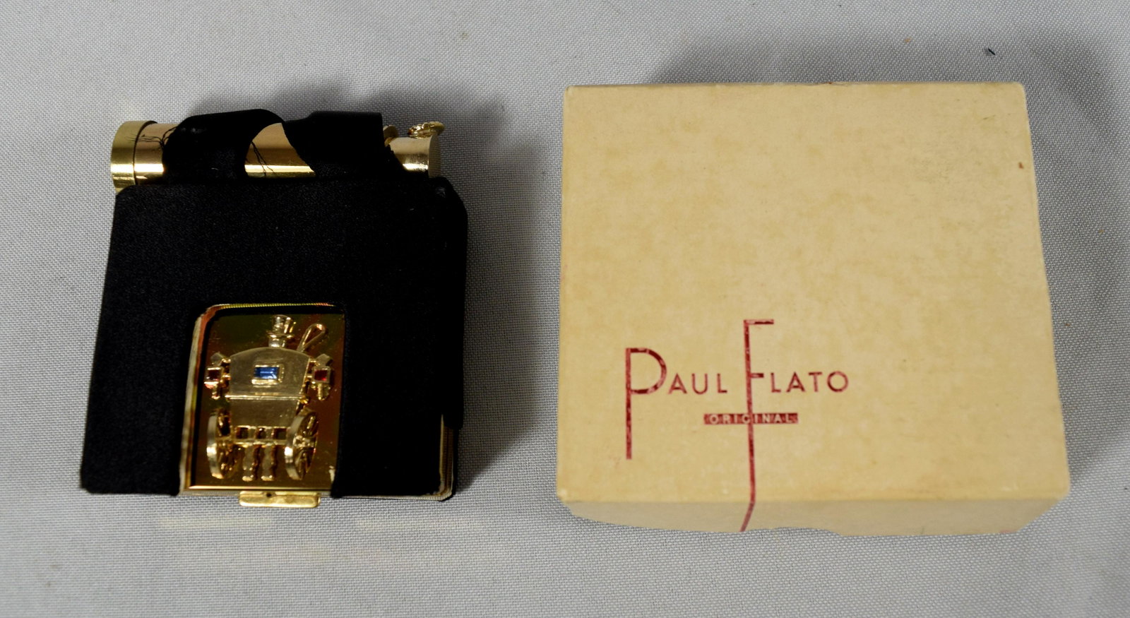 VINTAGE PAUL FLATO ORIGINAL COMPACT: : 1940s Paul Flato lipstick and compact in gold finish metal with jewel coach accent in holder. Measures 2 ½ inches x 2 ¼ inches. Original holder and box.
