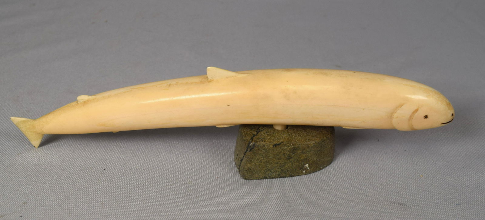 CARVED WHALE BONE FIGURE OF A SALMON FISH:: Measures 9 ½ inches long. Set on a green stone base.
