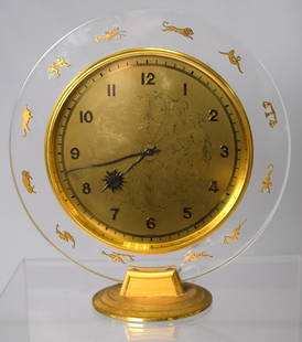 SWISS ZODIAC DESK CLOCK: C. Circular transparent lucite disk with applied gilt brass zodiac signs mounted on a circular brass stepped base. Roman numerals, serpentine sun hands. 15 jewels. 7 1/2 wide x 7 1/2 inches tall.