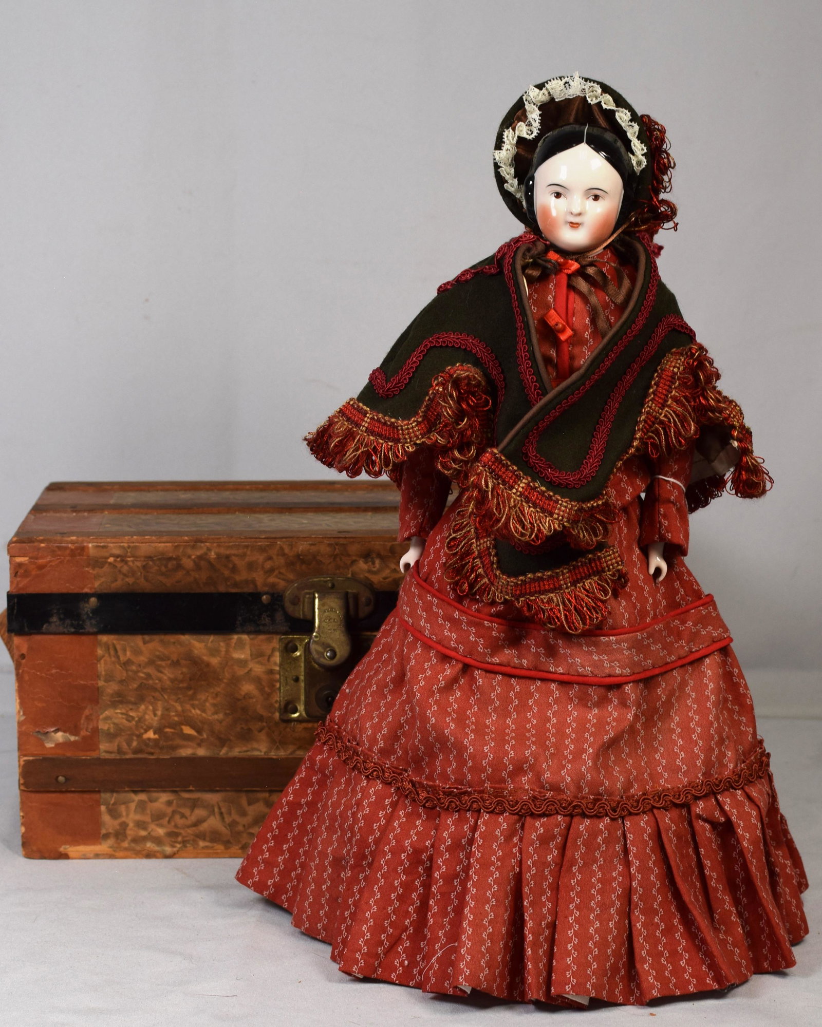 COVERED WAGON CHINA HEAD DOLL WITH ASSEMBLED TRUNK: Antique covered wagon china head doll with hand painted face and hair. 17 inches tall on stand with china hands,feet with hand painted boots and cloth body. Professionaly sewnsuit,undergarments,cape a