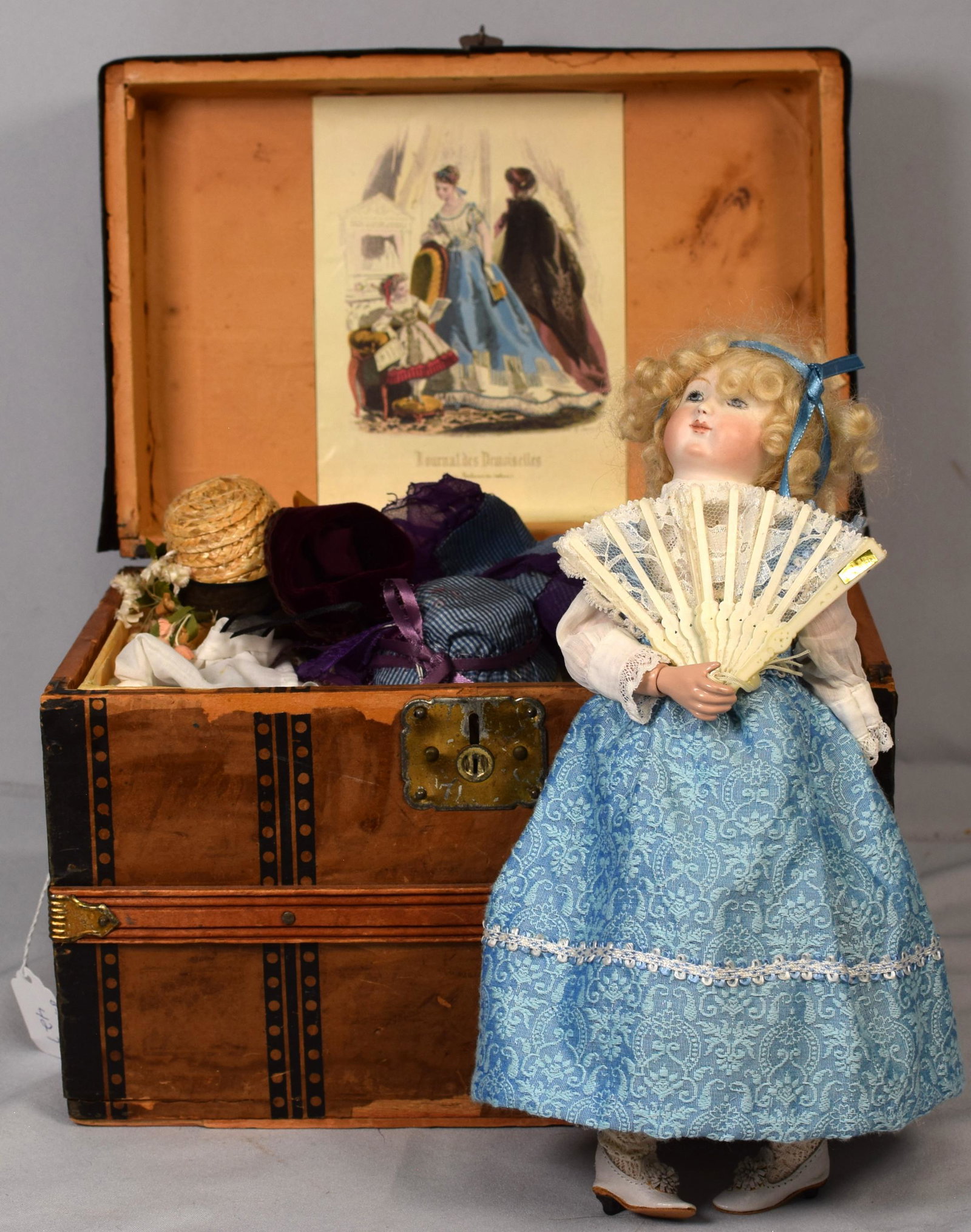 ANTIQUE DOLL TRUNK WITH REPRODUCTION DOLL: ca 19th century. Assembled Flat top wardrobe trunk with 18 hand made clothes pieces on bottom with made up tray top with hats and accessories. Good condition. 2) Reproduction bisque head doll withhand